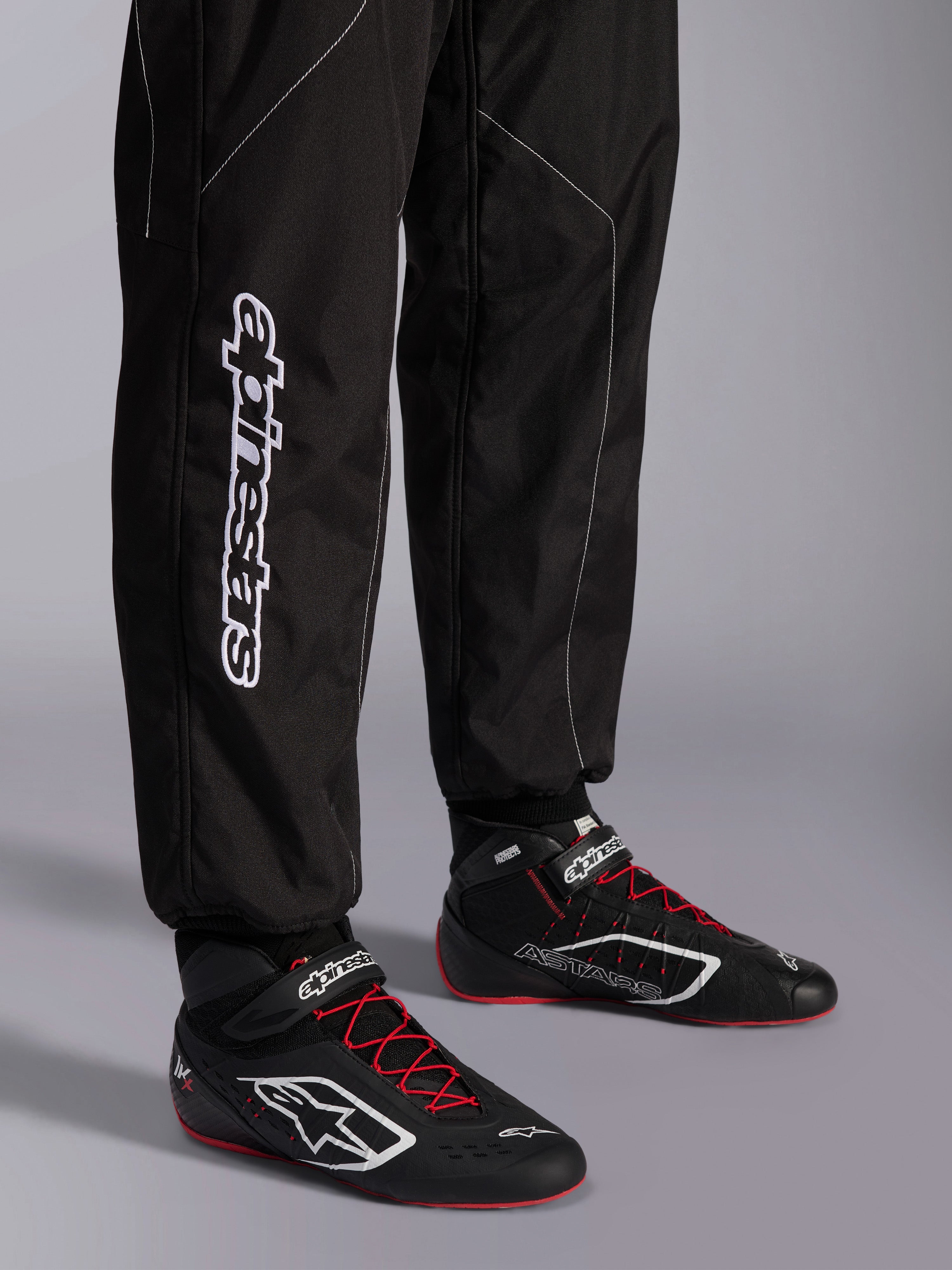 Alpinestars KMX-9 V3 dragt, kartingdragt, sort og hvid, detalje af underben med stort hvidt Alpinestars-branding, båret med sorte og røde racerstøvler, professionelt motorsportudstyr til karting
