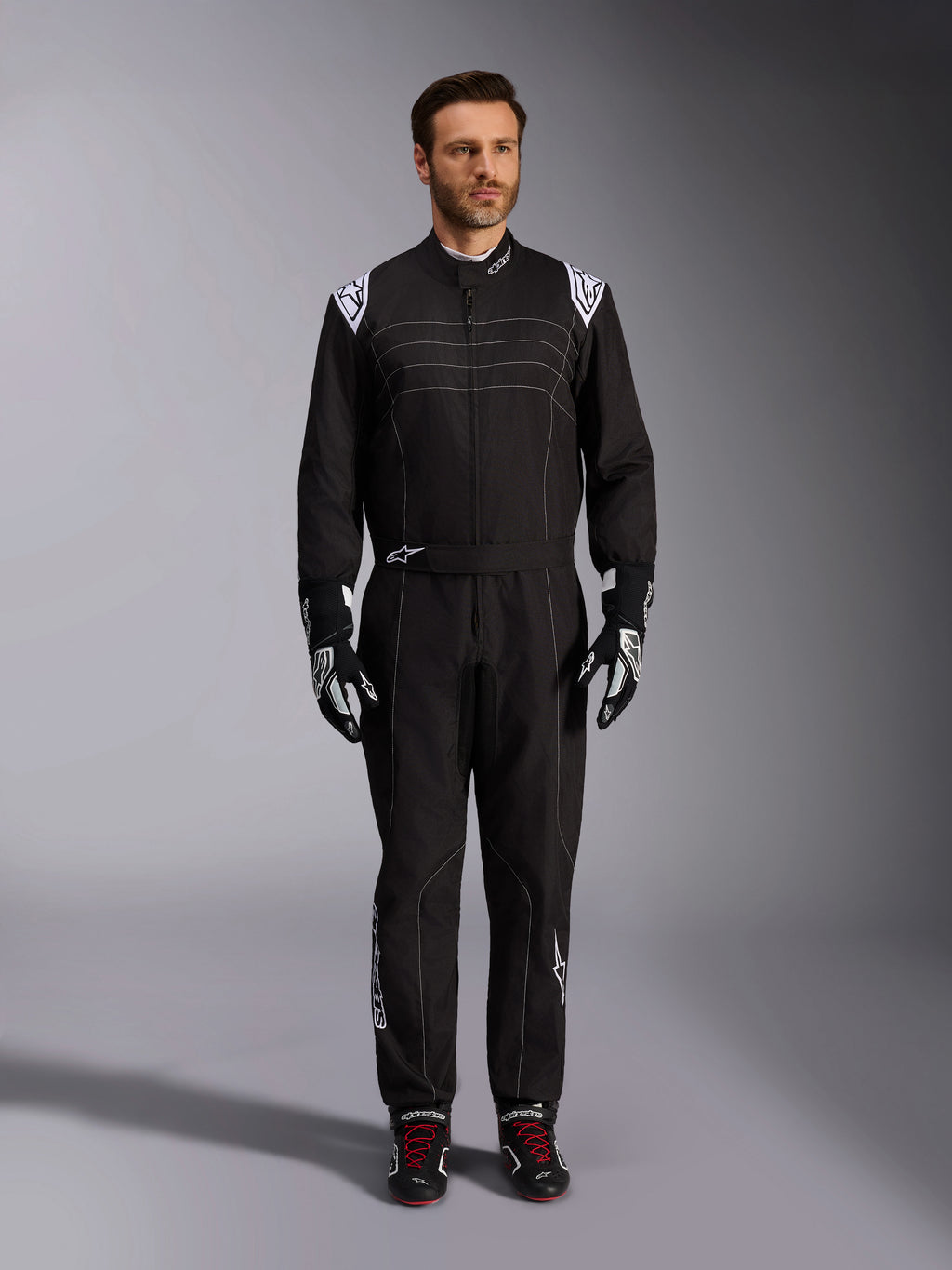 Alpinestars KMX-9 V3 dragt, sort og hvid kartingdragt, fuldlængde visning på en model, hvide skulderlogoer og detaljer, stylet med sort-hvide racinghandsker og sorte sko med røde snørebånd, atletisk-almindelig pasform til professionelt kartingudstyr.