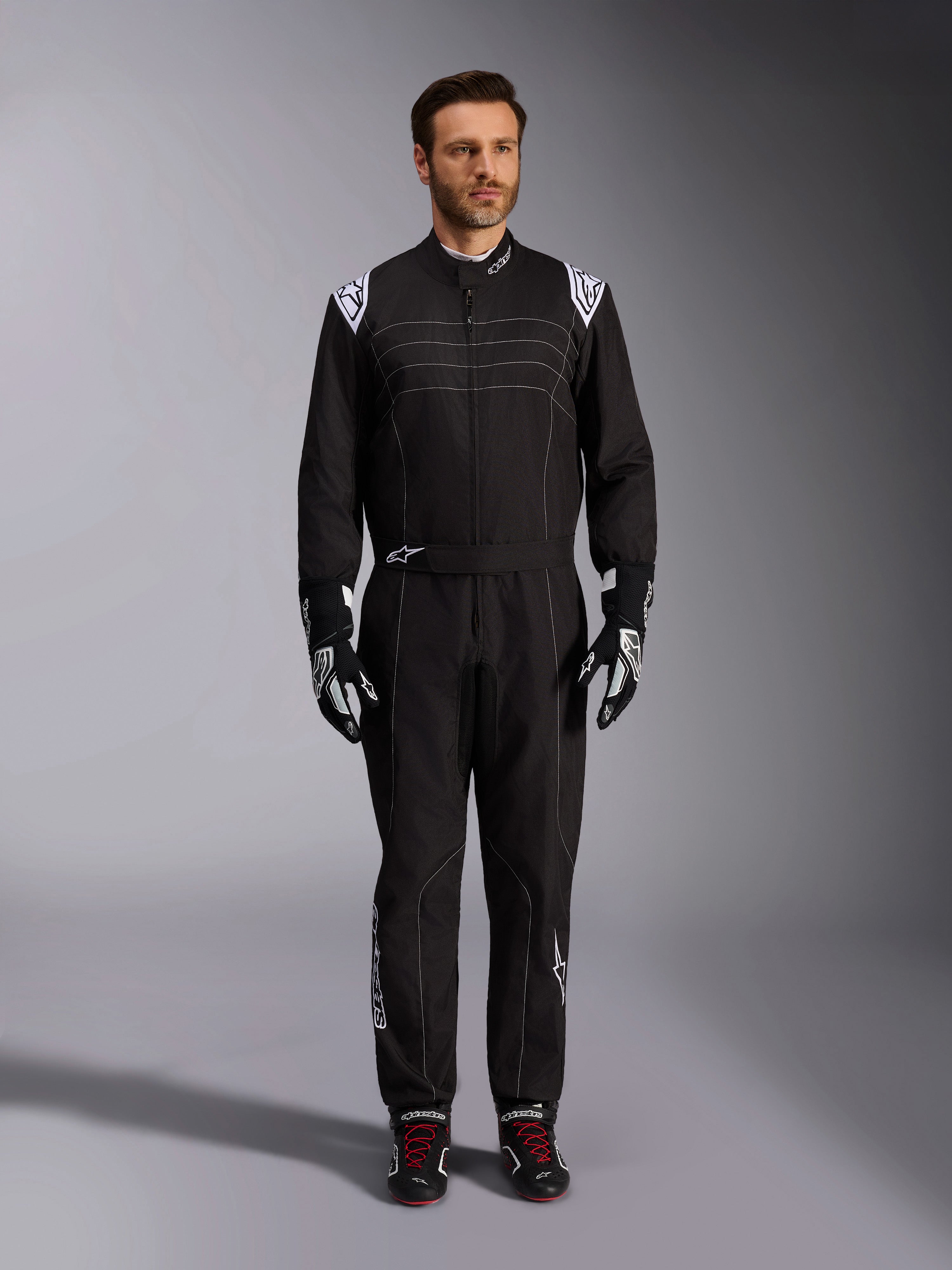 Alpinestars KMX-9 V3 dragt, sort og hvid kartingdragt, fuldlængde visning på en model, hvide skulderlogoer og detaljer, stylet med sort-hvide racinghandsker og sorte sko med røde snørebånd, atletisk-almindelig pasform til professionelt kartingudstyr.