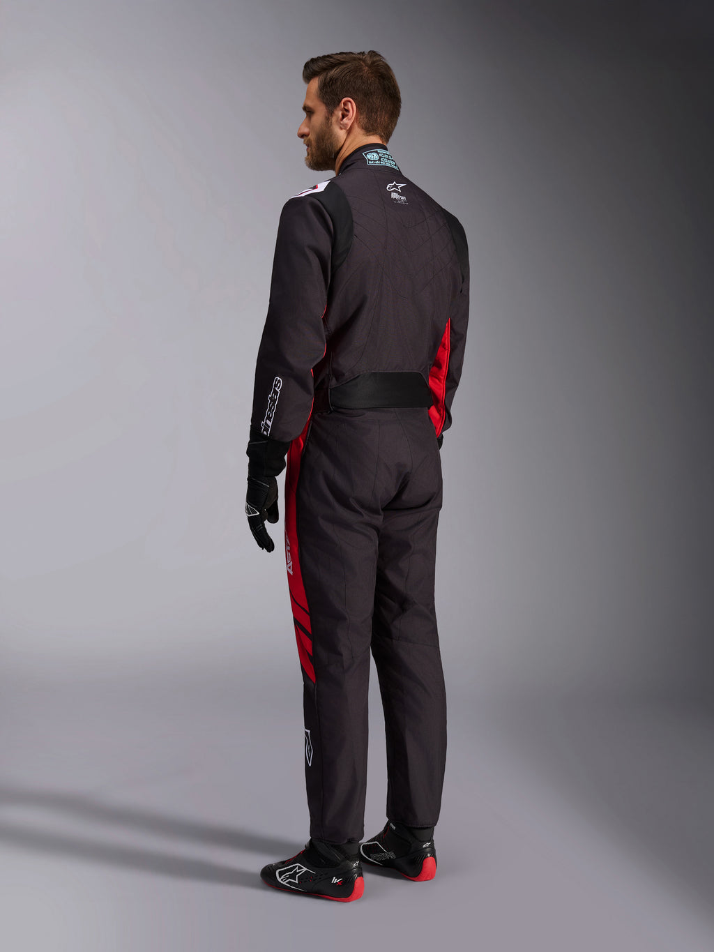 Alpinestars KMX-9 V3 Graphic 3 Suit, Black and Red, back view of model wearing full karting gear including black gloves and racing boots, featuring red side panels and white logo details