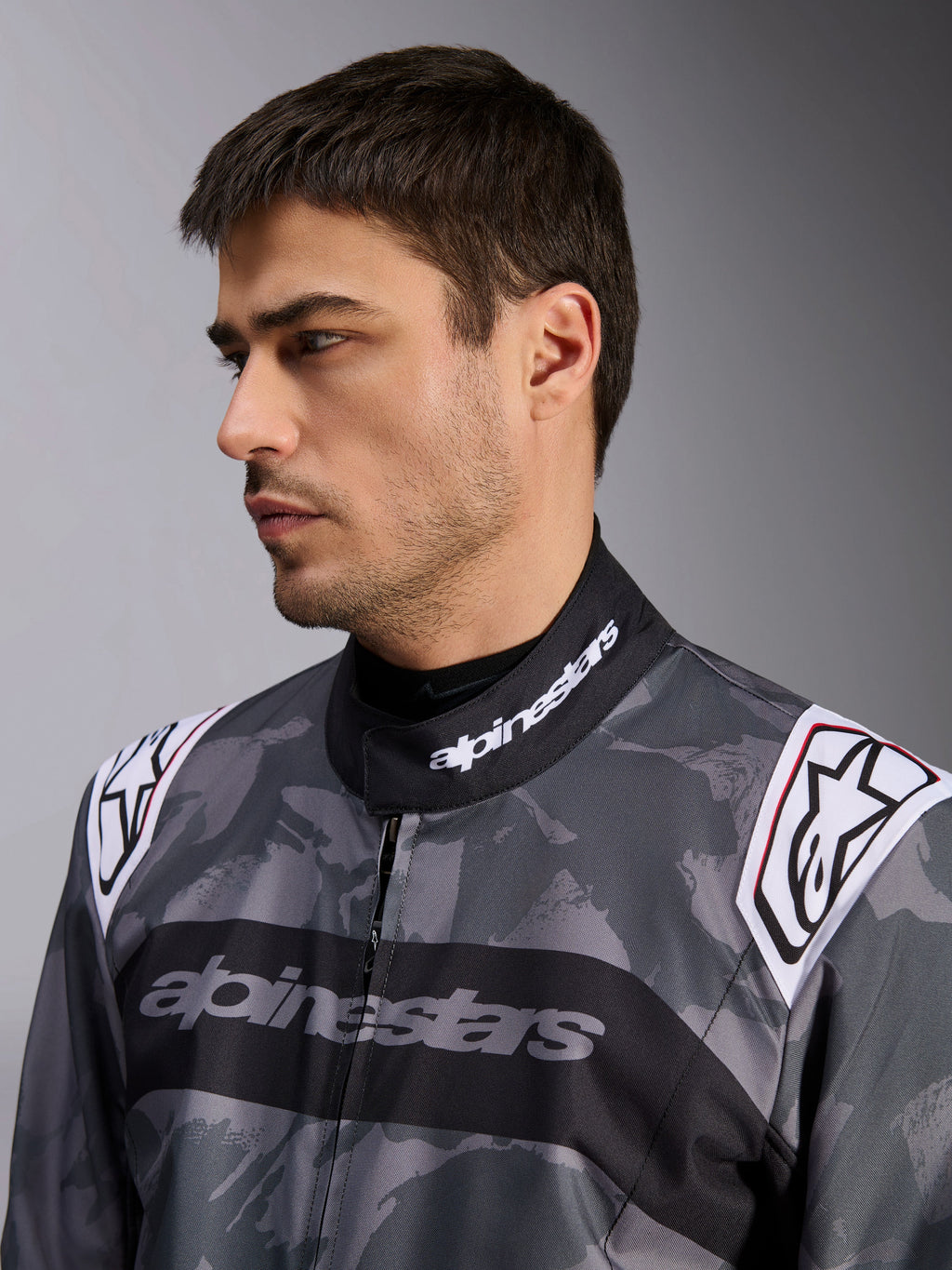 Alpinestars KMX-9 V3 Graphic 5 dragt, kartingdragt, mørkegråt og sort camouflagemønster, nærbillede af krave og skuldre med hvide logoer, professionel racerbeklædning