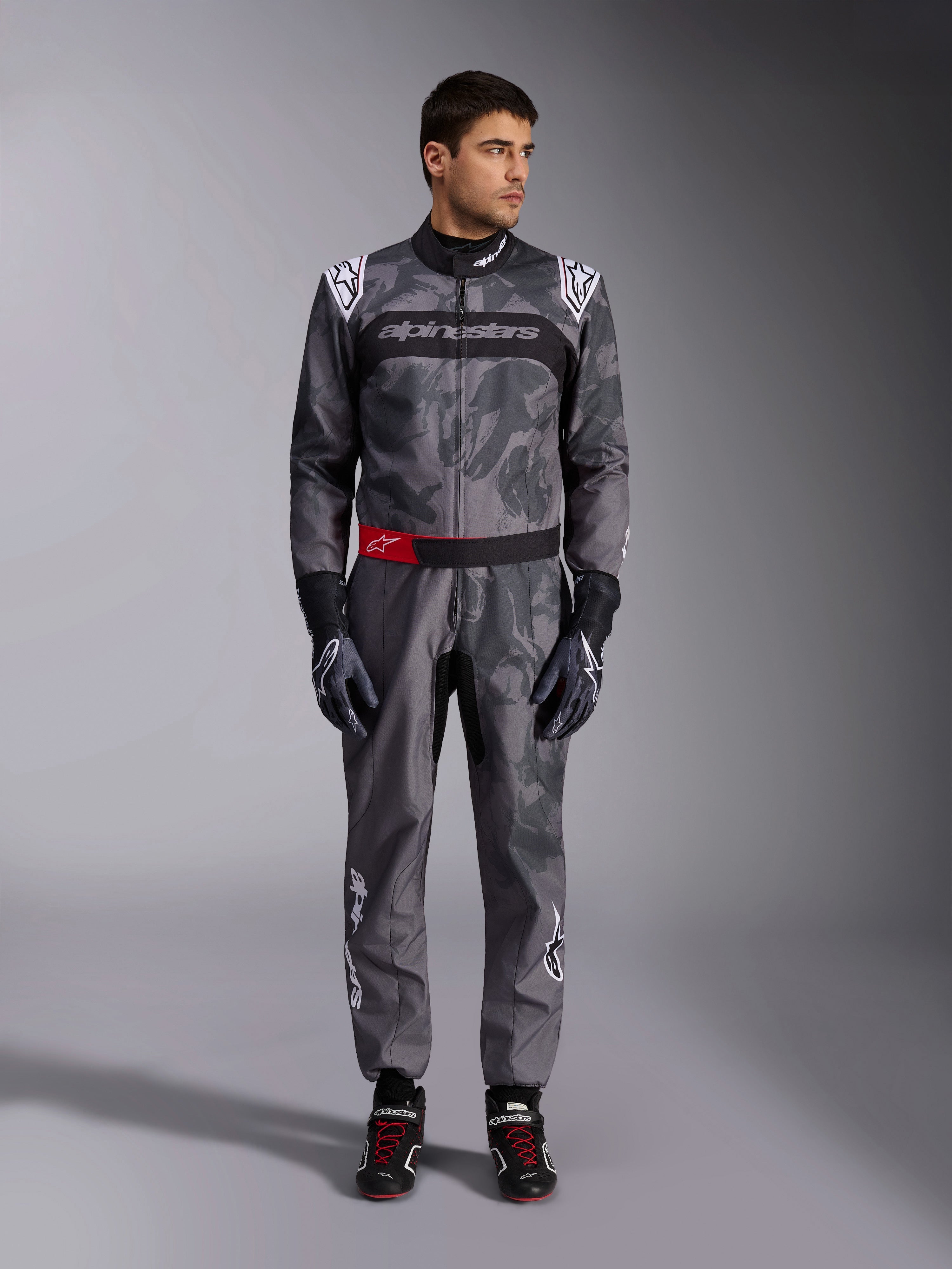 Alpinestars KMX-9 V3 Graphic 5 Suit, kartingdragt, mørkegrå og sort med grafik i camouflage-stil, med et sort brystbånd med hvidt logo og en rød taljebælte-accent, båret med matchende racerhandsker og sko, professionelt motorsportudstyr