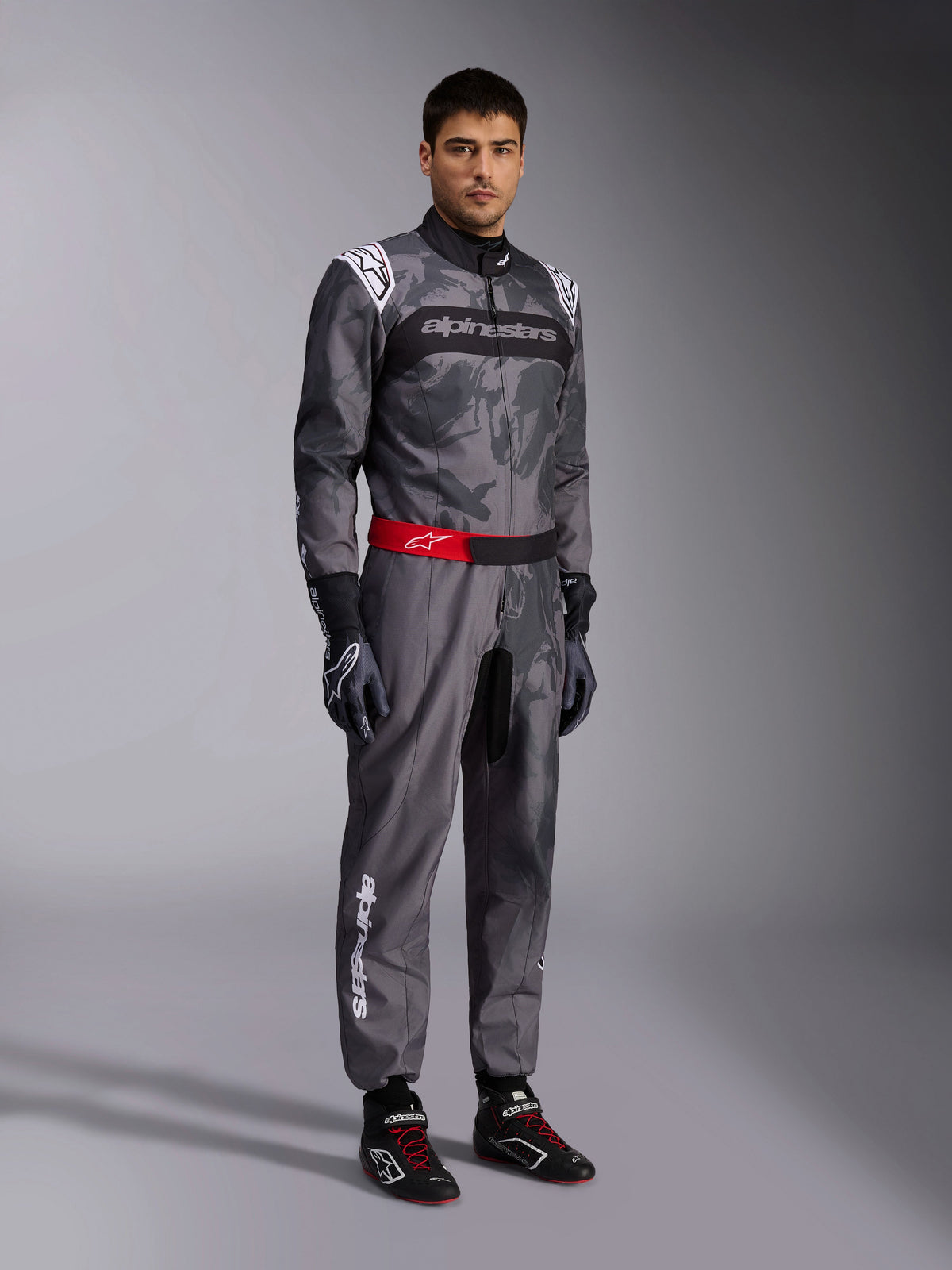 Alpinestars KMX-9 V3 Graphic 5 dragt, kartingdragt, mørkegrå og sort med camo-grafisk mønster, rødt taljebælte med hvidt logo, båret med racerhandsker og -sko, professionelt motorsportsudstyr til karting