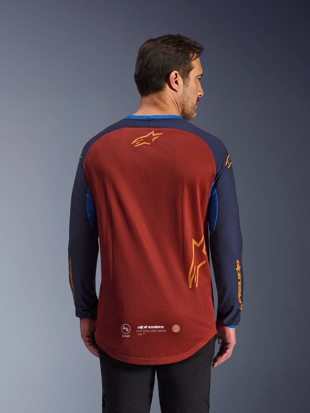Alpinestars Maxdura Dual Jersey i Rust Brown og Mood Indigo, set bagfra, åndbar mesh-torso, mørkeblå ærmer med orange Alpinestars-branding og forlænget bagkant for ekstra dækning.