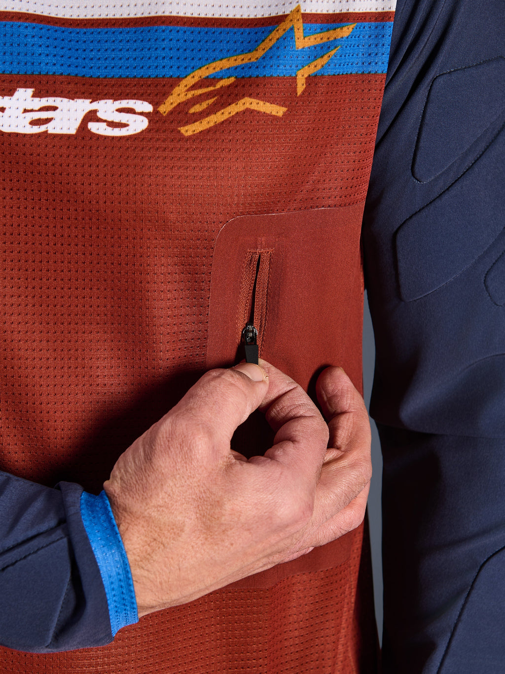 Nærbillede af Alpinestars Maxdura Dual Jersey, rustbrun mesh-torso med sømløs lynlåslomme på brystet, Mood Indigo-ærmer med integreret polstring, teknisk adventure-motorcykeltrøje-detalje