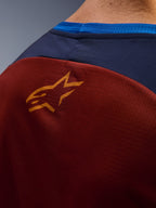 Nærbillede af Alpinestars Maxdura Dual Jersey, rustbrunt mesh-stof på ryggen, lille orange stjernelogo, mørkeblåt øvre panel og lyseblå kravekant, detaljeret visning af adventure-motorcykeltrøje