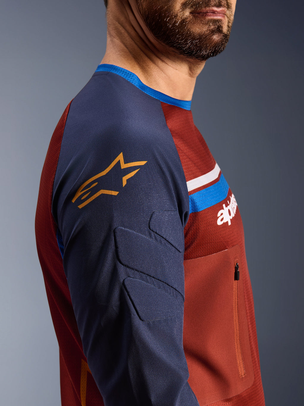 Alpinestars Maxdura Dual Jersey, Rust Brown og Mood Indigo, sideprofilvisning, polstrede ærmer med gult stjernelogo, mesh-torso-konstruktion med brystlomme med lynlås, teknisk motorcykelbeklædning til adventure-kørsel