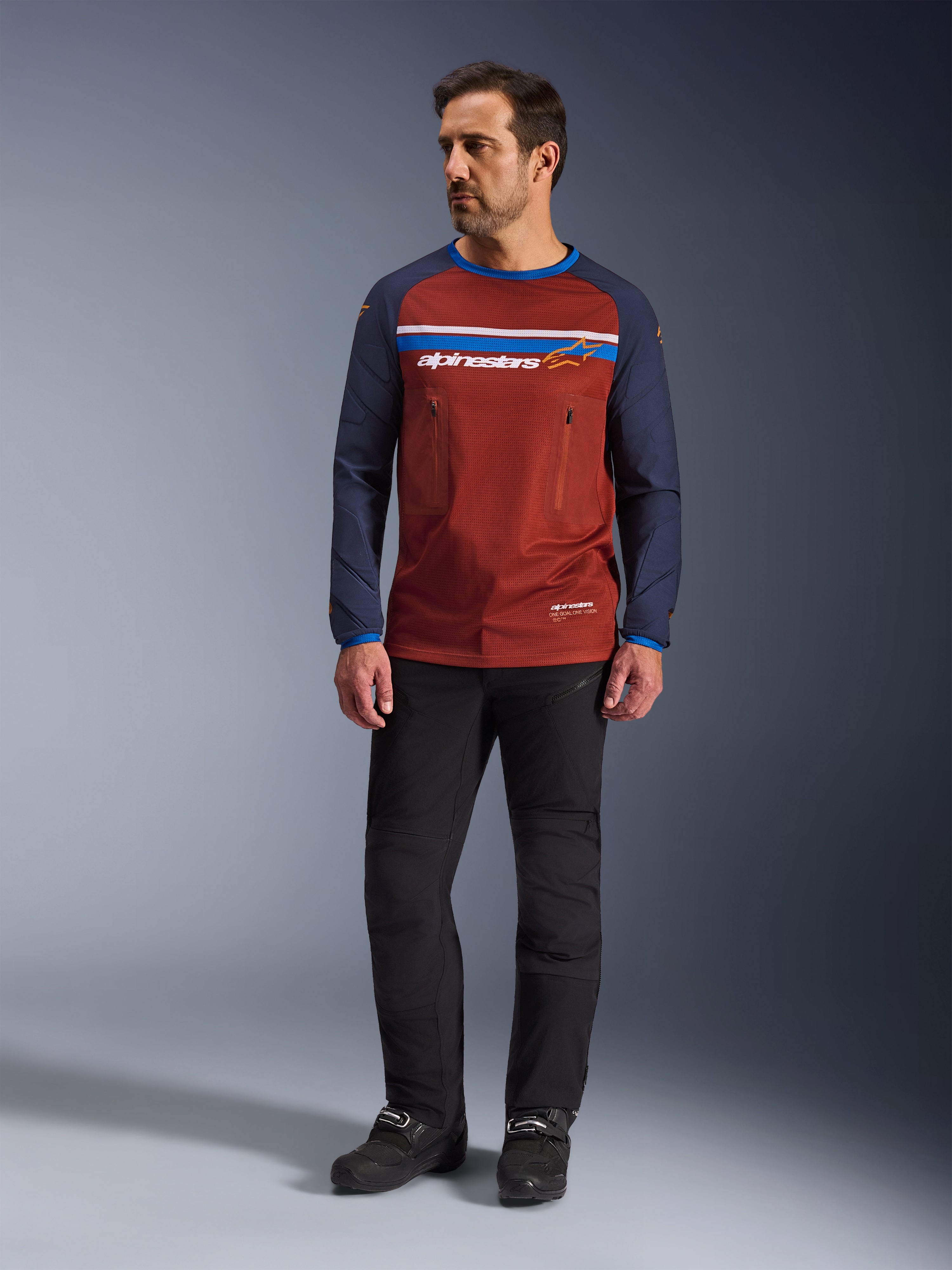 Alpinestars Maxdura Dual Jersey, Rust Brown og Mood Indigo, adventure motorcykeltrøje med en mesh-torso og navyblå ærmer, båret af en model med sorte kørebukser og sorte støvler, teknisk dual-sport-beklædning til off-road kørsel