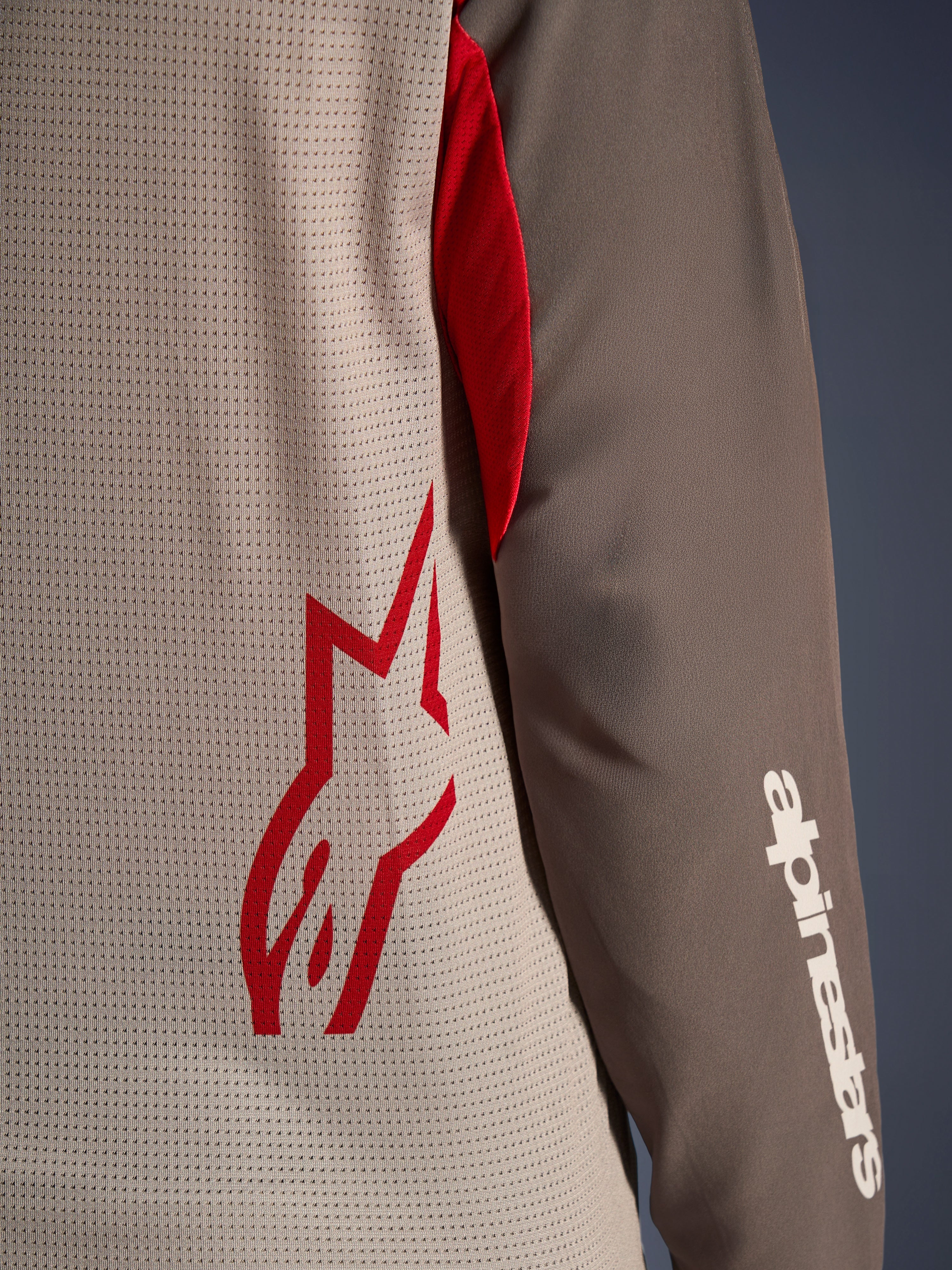 Alpinestars Maxdura Dual Jersey, Aluminum Walnut, nærbillede der viser den ventilerede mesh-torso med et rødt stjernelogo og et brunt slidstærkt ærme med et hvidt Alpinestars-navnetræk, teknisk beklædning til adventure- og dual-sport-motorcykelkørsel