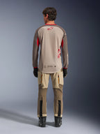 Alpinestars Maxdura Dual Jersey i Aluminum Walnut, set bagfra, beige mesh-overkrop med brune ærmer og røde logoer, forlænget bagkant, kombineret med adventure-kørebukser og sorte støvler.