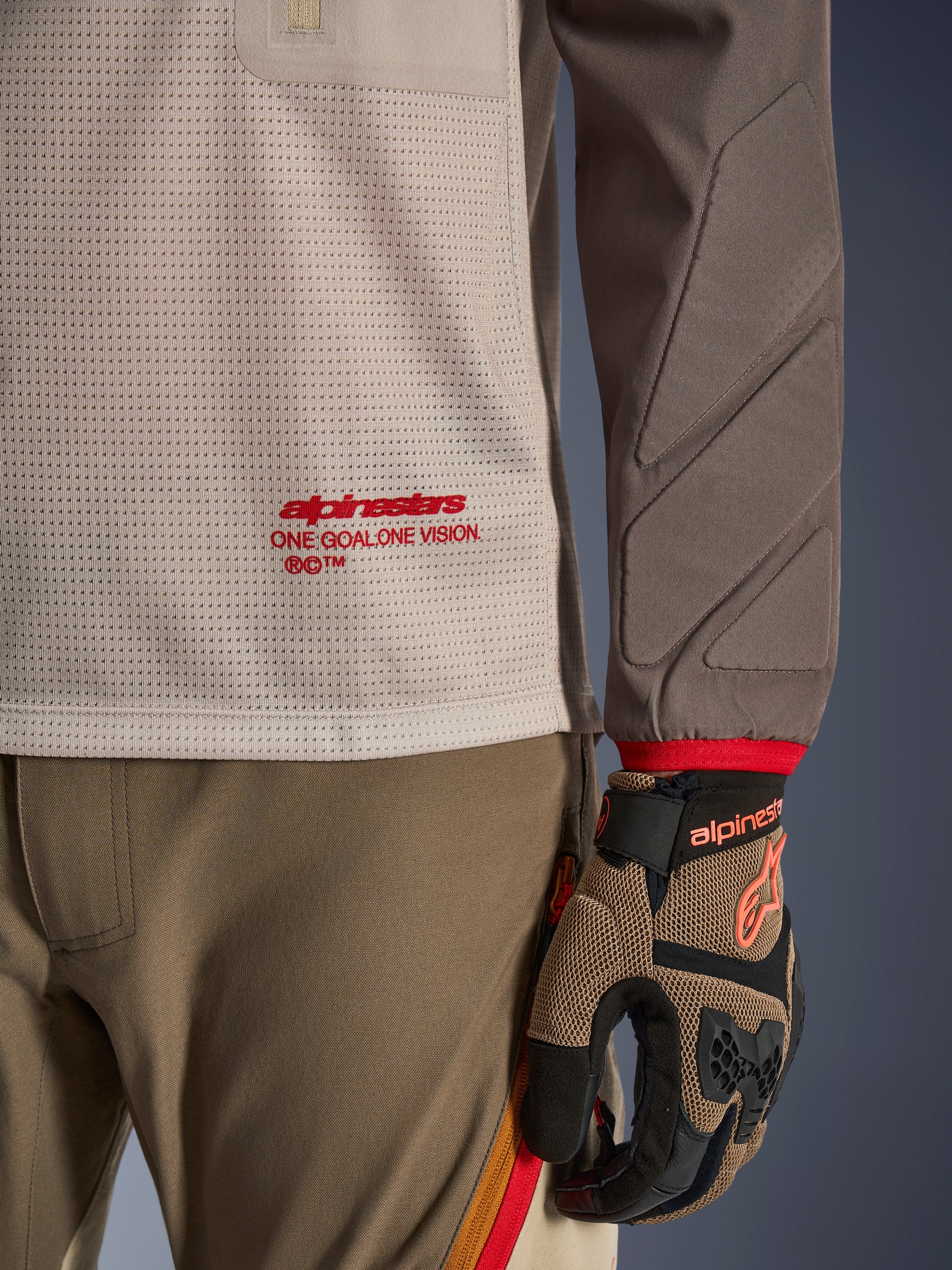 Alpinestars Maxdura Dual Jersey i Aluminum Walnut, detaljeret visning af den ventilerede mesh-overkrop med rød branding, slidstærkt ærme med integreret polstring, båret med koordinerede adventure-kørebukser og handsker