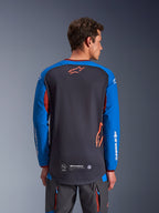 Alpinestars Maxdura Dual Jersey i Deep Gray og Royal Blue, rygvisning af mandlig model, mesh-konstruktion på torso med orange Astars-logo, lange ærmer med hvid branding, bordeauxrød krave og manchetter, båret med grå tekniske bukser, dual-sport og adventure motorcykeludstyr