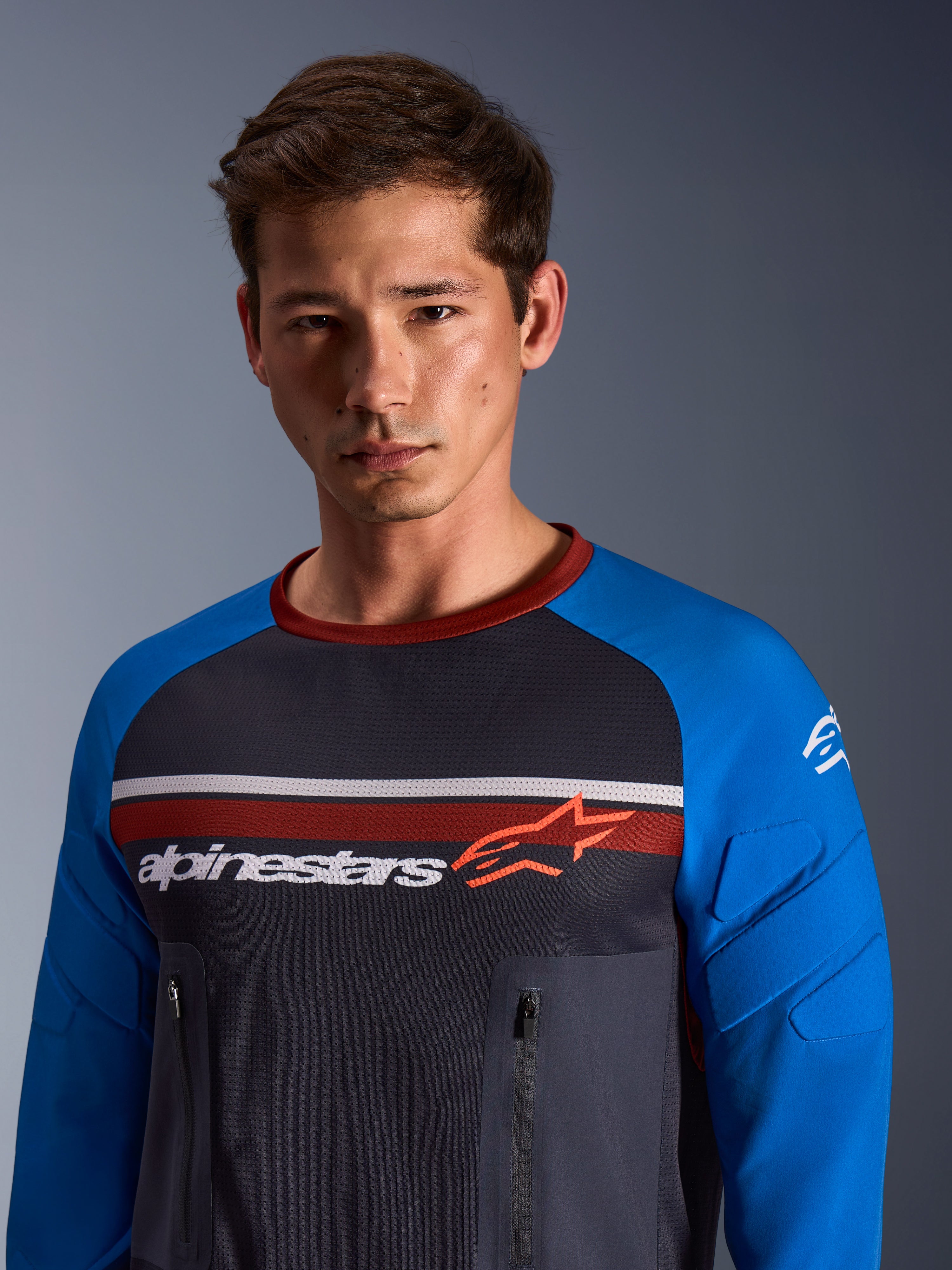 Alpinestars Maxdura Dual Jersey, mørkegrå og kongeblå, båret af en mandlig model, med mesh-torso, kongeblå ærmer med integreret polstring og lodrette brystlommer med lynlås med Alpinestars-branding over brystet.