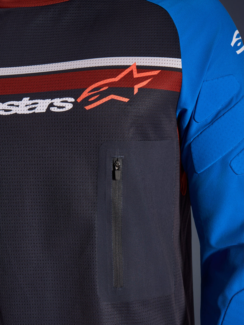 Alpinestars Maxdura Dual Jersey, nærbillede af bryst og ærme, mørkegrå og kongeblå, brystlomme med lynlås, åndbar mesh-overkrop og integreret polstring på ærmerne, Alpinestars-logo over røde og hvide striber.