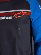 Alpinestars Maxdura Dual Jersey, nærbillede af bryst og ærme, mørkegrå og kongeblå, brystlomme med lynlås, åndbar mesh-overkrop og integreret polstring på ærmerne, Alpinestars-logo over røde og hvide striber.