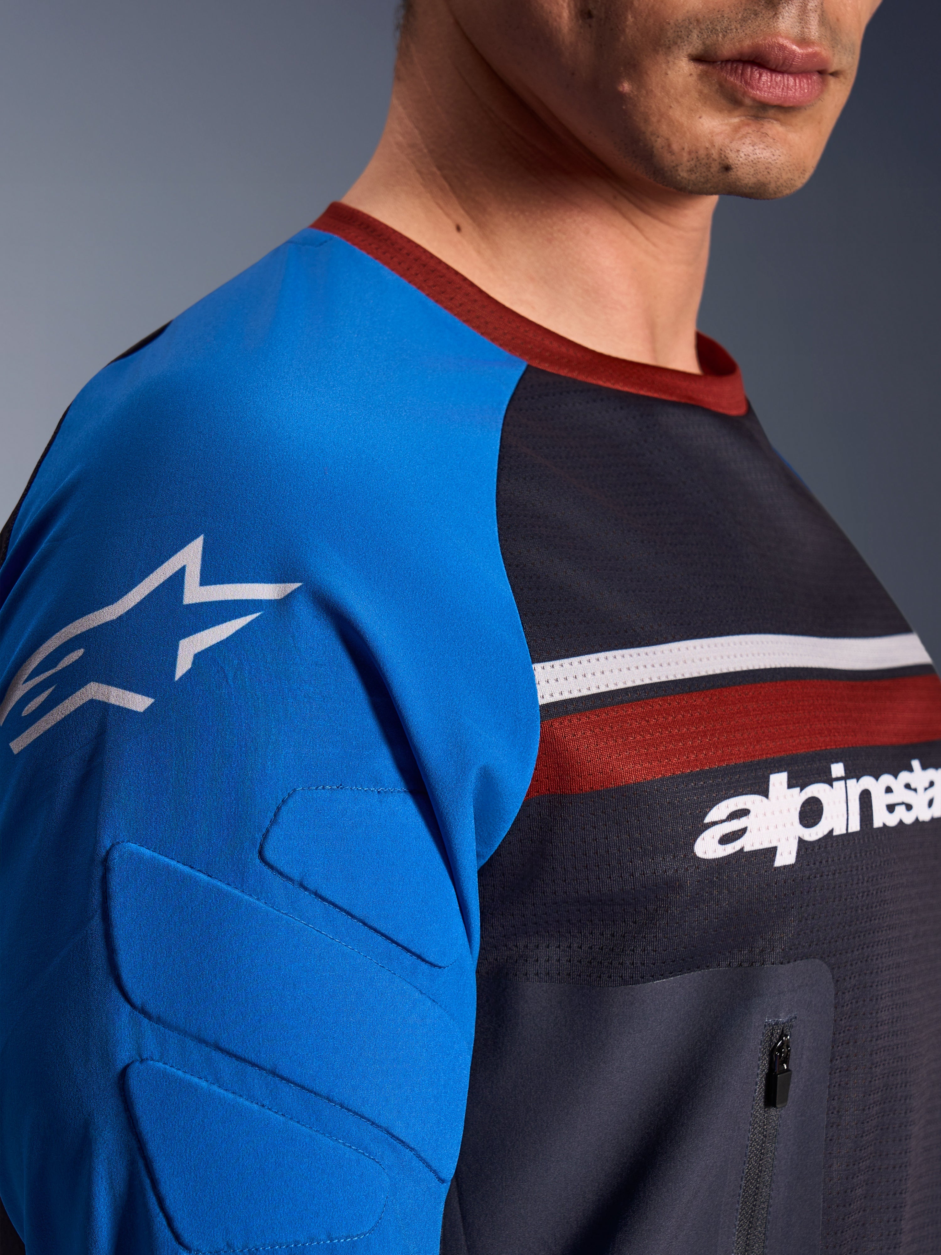 Alpinestars Maxdura Dual Jersey, motorcykeltrøje, mørkegrå og kongeblå, nærbillede der viser brystlomme med lynlås, mesh-materiale på overkroppen og integreret polstring på ærmerne med stjernelogo