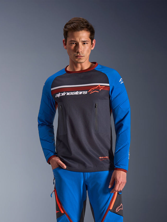 Mand iført Alpinestars Maxdura Dual Jersey i Deep Gray og Royal Blue med orange detaljer, med fuld mesh-overkrop og brystlommer med lynlås, kombineret med matchende blå adventure-kørebukser, teknisk dual-sport og off-road beklædning