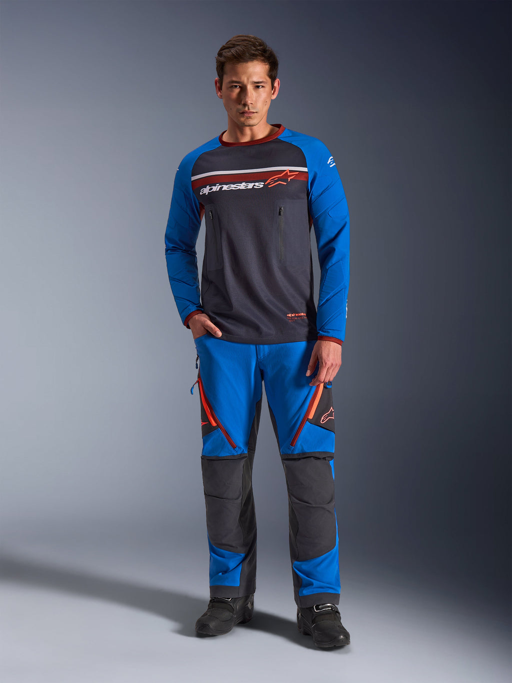 Alpinestars Maxdura Dual jersey, motorcykeltrøje, mørkegrå og kongeblå, overkrop i fuld mesh med polstrede ærmer og brystlommer med lynlås, med hvidt og orange Alpinestars-logo, bæres med matchende adventure-bukser og sorte støvler