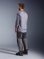 Mand iført Alpinestars Maxdura Dual Jersey, lysegrå med røde Alpinestars-logoer, set bagfra, viser mesh-overkrop og lange ærmer, kombineret med mørkegrå tekniske bukser og sorte motorcykelstøvler