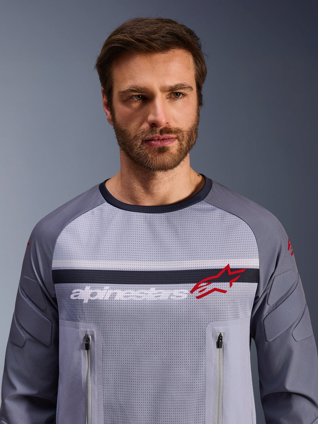 Alpinestars Maxdura Dual Jersey, mellemgrå og mørkegrå, båret af mandlig model, med mesh-torso til ventilation, dobbelte lynlåslommer på brystet, hvidt 'alpinestars'-branding og rødt stjernelogo, performance off-road adventure-udstyr