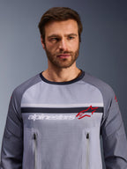 Alpinestars Maxdura Dual Jersey, mellemgrå og mørkegrå, båret af mandlig model, med mesh-torso til ventilation, dobbelte lynlåslommer på brystet, hvidt 'alpinestars'-branding og rødt stjernelogo, performance off-road adventure-udstyr