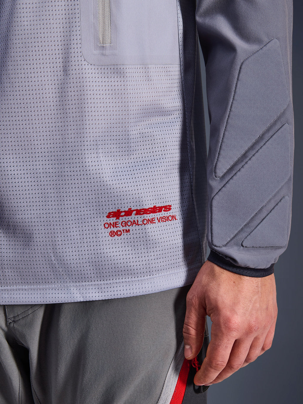 Alpinestars Maxdura Dual Jersey, mellemgrå og mørkegrå, nærbillede der viser åndbar mesh-torso med rød branding, detalje med lynlåslomme og integreret polstring på ærmet, teknisk adventure-motorcykeludstyr