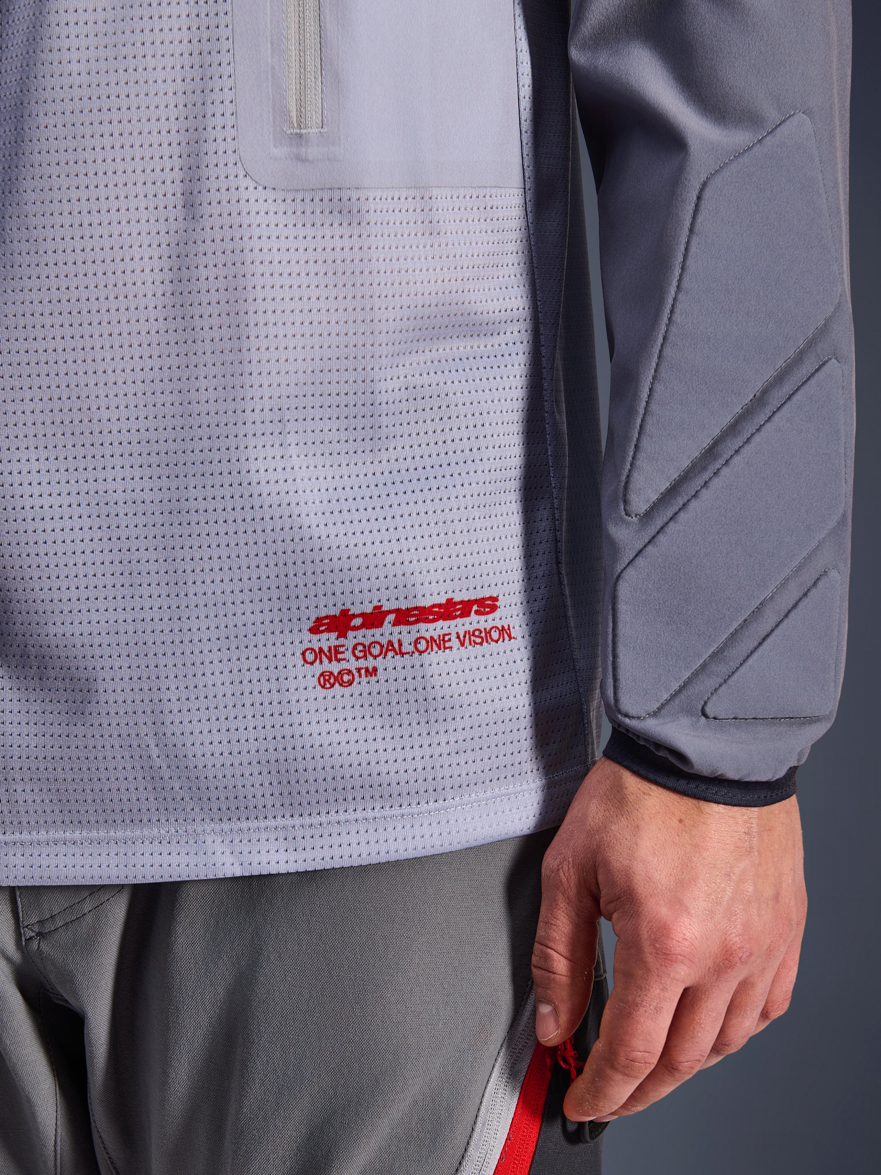Alpinestars Maxdura Dual Jersey, mellemgrå og mørkegrå, nærbillede der viser åndbar mesh-torso med rød branding, detalje med lynlåslomme og integreret polstring på ærmet, teknisk adventure-motorcykeludstyr