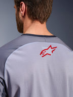 Alpinestars Maxdura Dual Jersey i mellemgrå og mørkegrå, nærbillede af den øverste del af ryggen og kraven, lille rødt Alpinestars-stjernelogo på åndbart lysegråt mesh-stof, mørkegrå kant ved halsen, designet til adventure- og off-road-kørsel