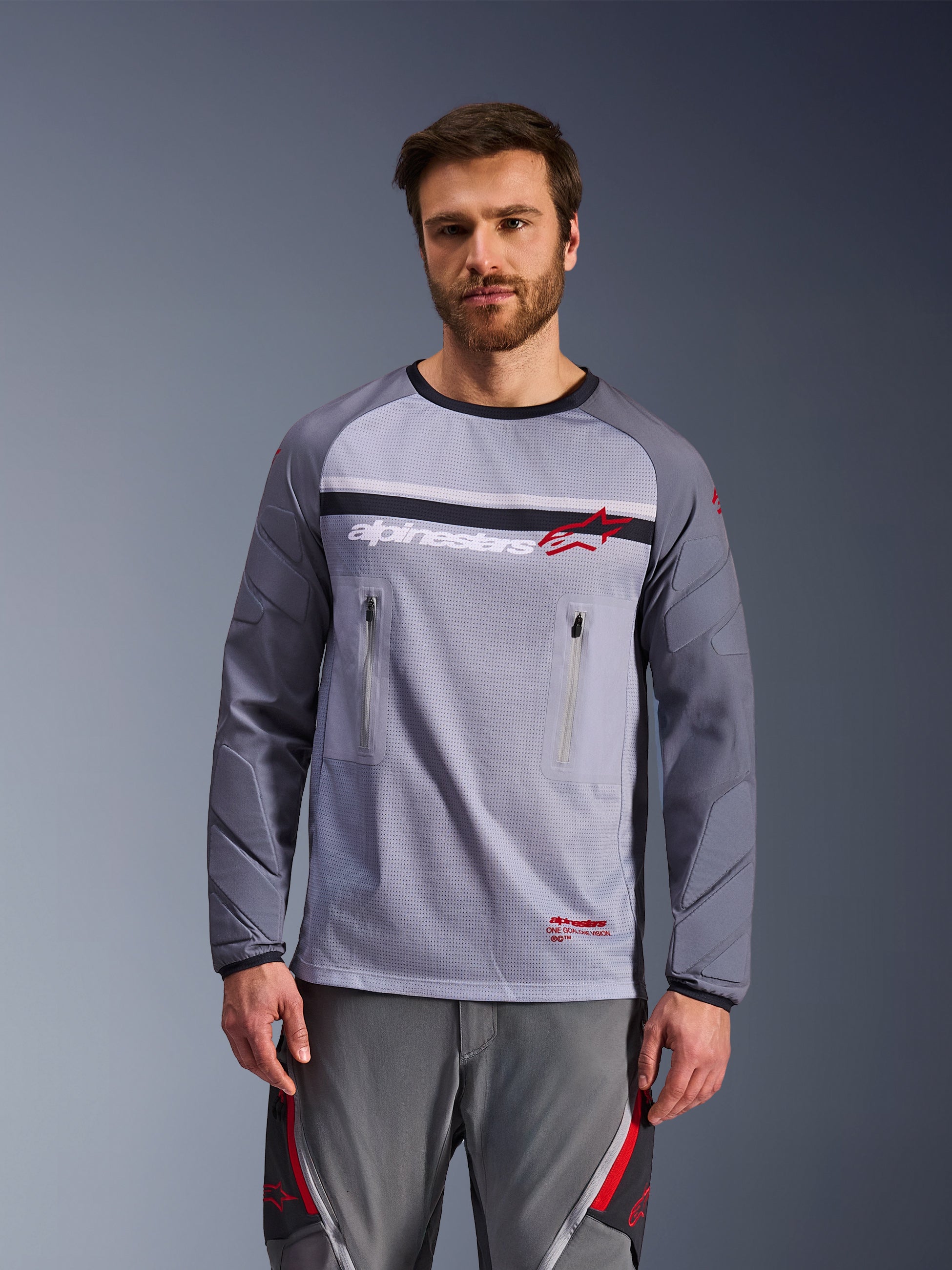 Alpinestars Maxdura Dual Jersey, mellemgrå og mørkegrå, båret af en model med matchende grå bukser, med brystlommer med lynlås, mesh-overkrop og polstrede, slidstærke ærmer, adventure motorcykel off-road udstyr