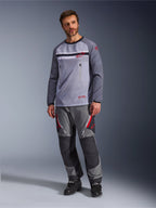 En mand iført Alpinestars Maxdura Dual Jersey i mellemgrå og mørkegrå, stylet med matchende grå og sorte adventure-bukser og sorte støvler, med en åndbar mesh-overkrop, brystlommer med lynlås og røde logo-detaljer.