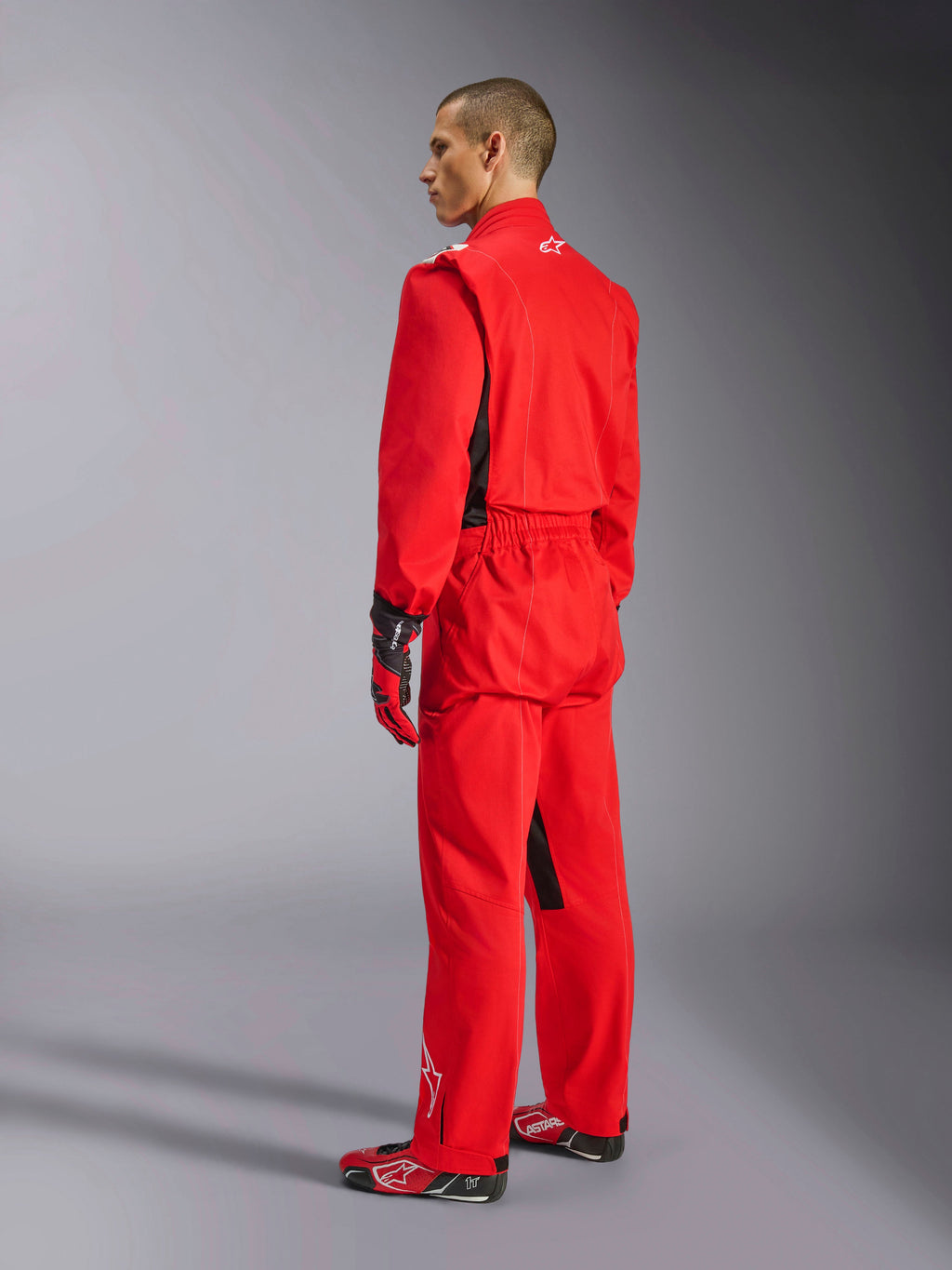 Alpinestars Kart Indoor V2 Suit, rød karting-køredragt, set bagfra fra siden på en model, båret med matchende røde handsker og racersko, enkeltlags poly-bomuldstwill-konstruktion, professionelt motorsportudstyr til indendørs karting