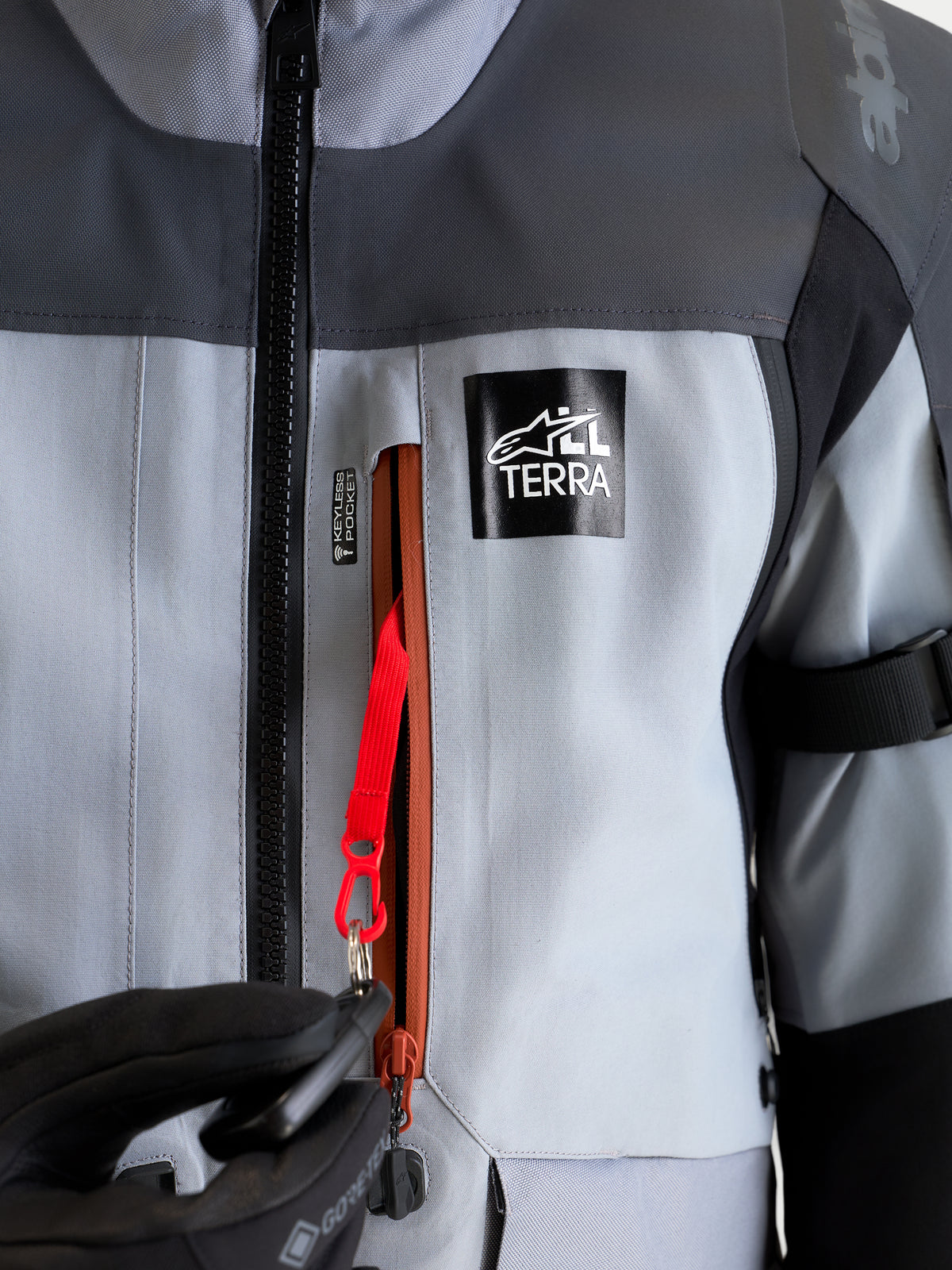 Alpinestars St-7 V2 2L Gore-Tex jakke, adventure-motorcykeljakke i grå og sort, nærbillede af den vandtætte nøglefri lomme med rød fastgørelsessnor og All Terra-branding