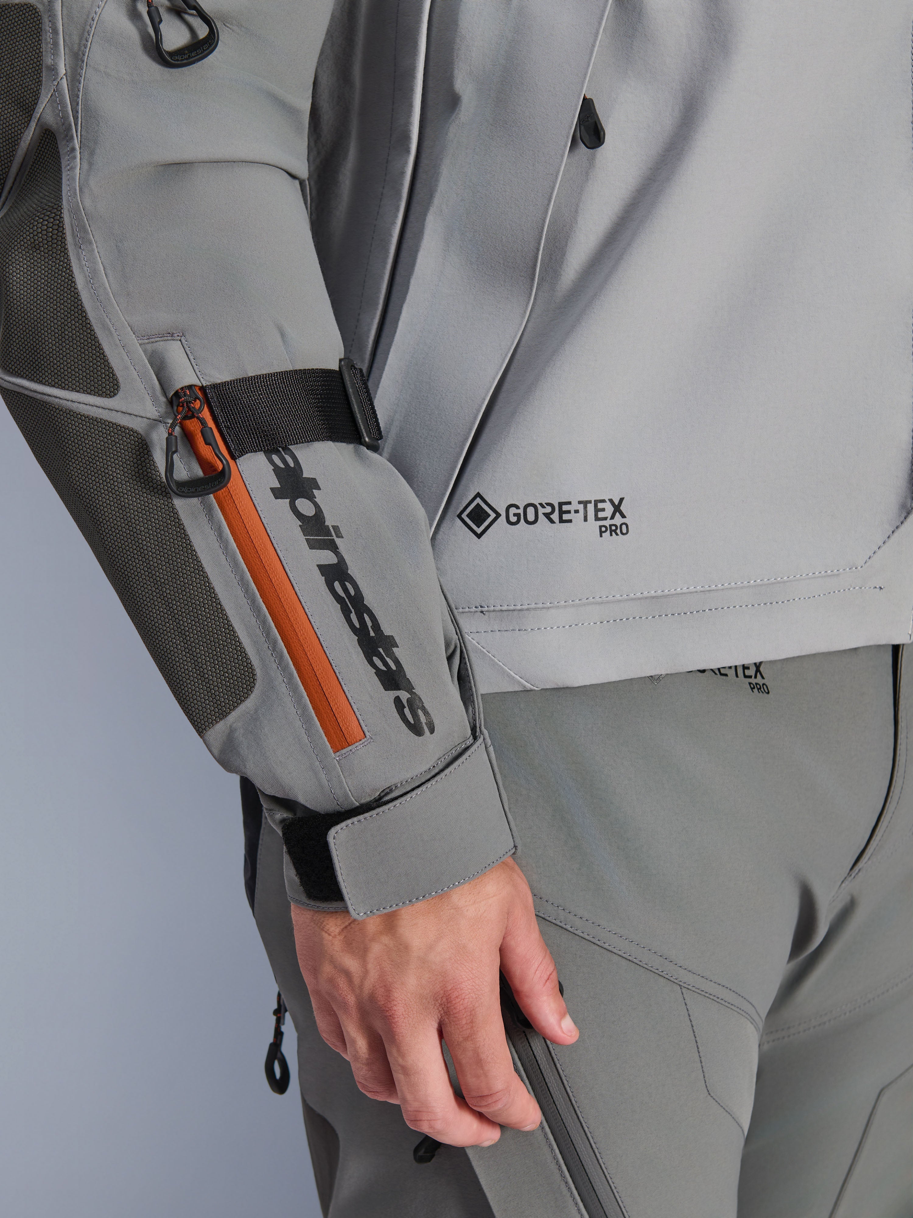 Alpinestars Nazca 3L GORE-TEX PRO jakke, mørkegrå og mellemgrå adventure-jakke, nærbillede af ærme med sort branding og orange lynlåsdetalje, GORE-TEX PRO-logo på torso, holdbar tekstilkonstruktion med forstærket albuepanel