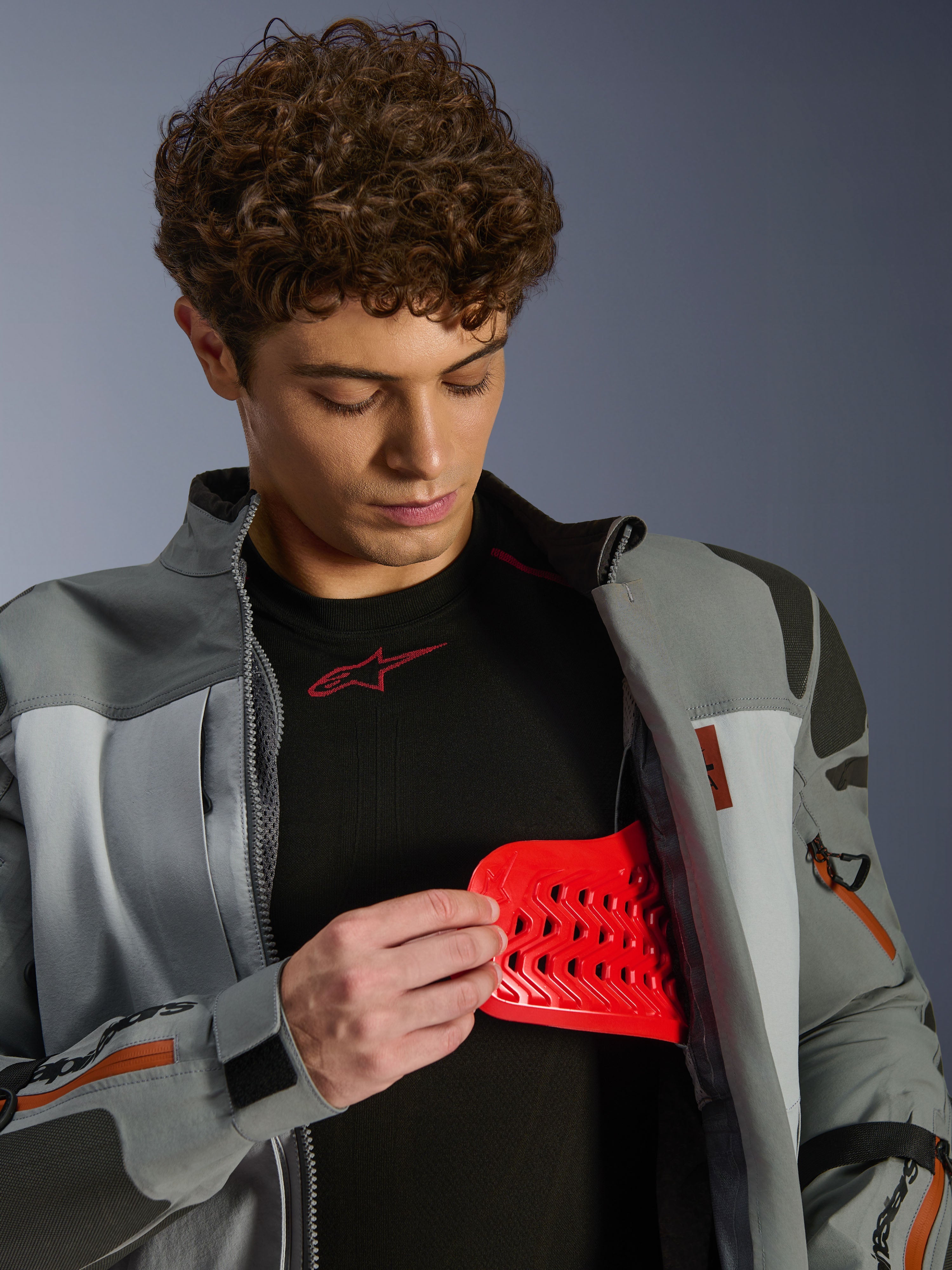 Mandlig model iført Alpinestars Nazca 3L GORE-TEX PRO Jakke, mørkegrå og mellemgrå, viser rød Nucleon PLASMA Pro-beskyttelsesindsats, adventure-køreudstyr, premium motorcykeljakke med tekniske detaljer