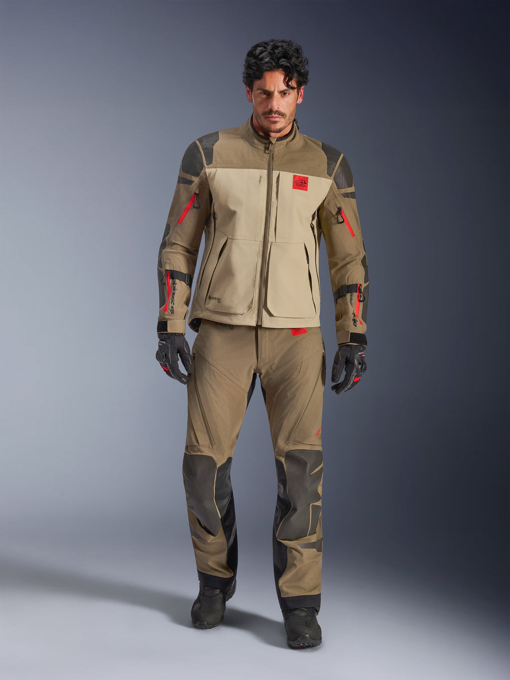 Alpinestars Nazca 3L GORE-TEX PRO jakke, Walnut Rock Brown, adventure-motorcykeljakke båret med matchende bukser og handsker, røde lynlåsdetaljer, 'All Terra' brystlogo og robust tekstilkonstruktion.
