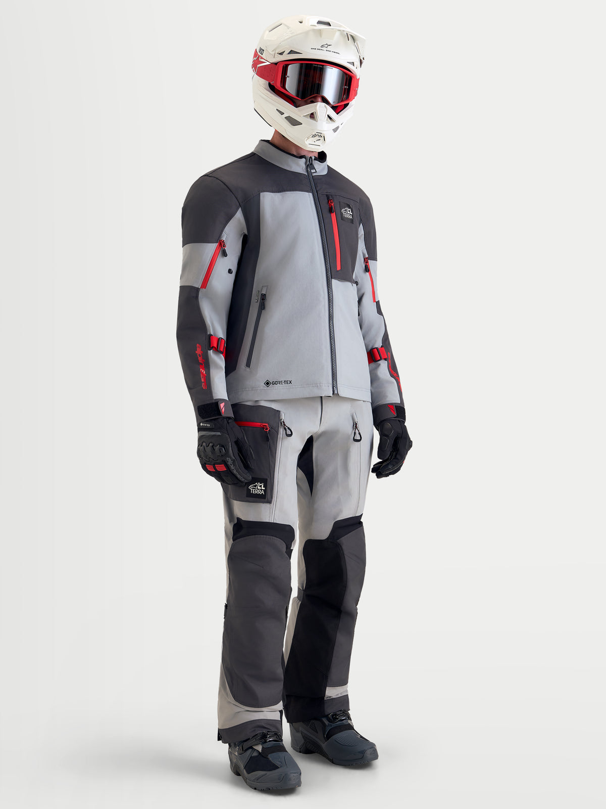 Alpinestars Arenis Gore-Tex udstyrssæt, herre adventure-motorcykeljakke og -bukser i grå, mørkegrå og rød, set i fuld figur på en model iført matchende hjelm, goggles, handsker og støvler, vandtæt terrænkøretøj