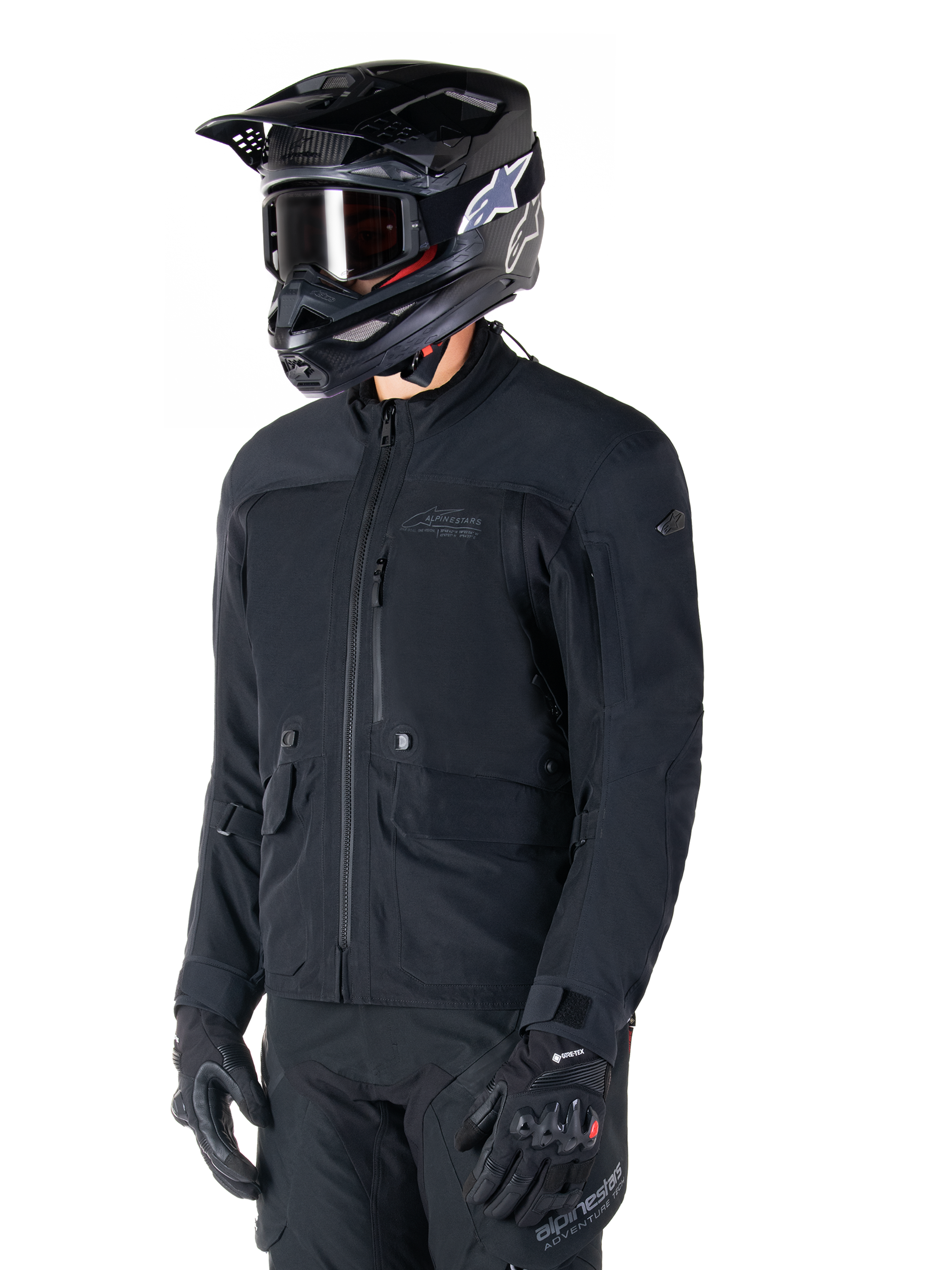 Alpinestars St-7 Prime GORE-TEX-jakke, sort motorcykeljakke, båret af en rytter med sort hjelm og beskyttelsesbriller, med store cargolommer på brystet og en lamineret vandtæt skal, premium udstyr til adventure touring og pendling