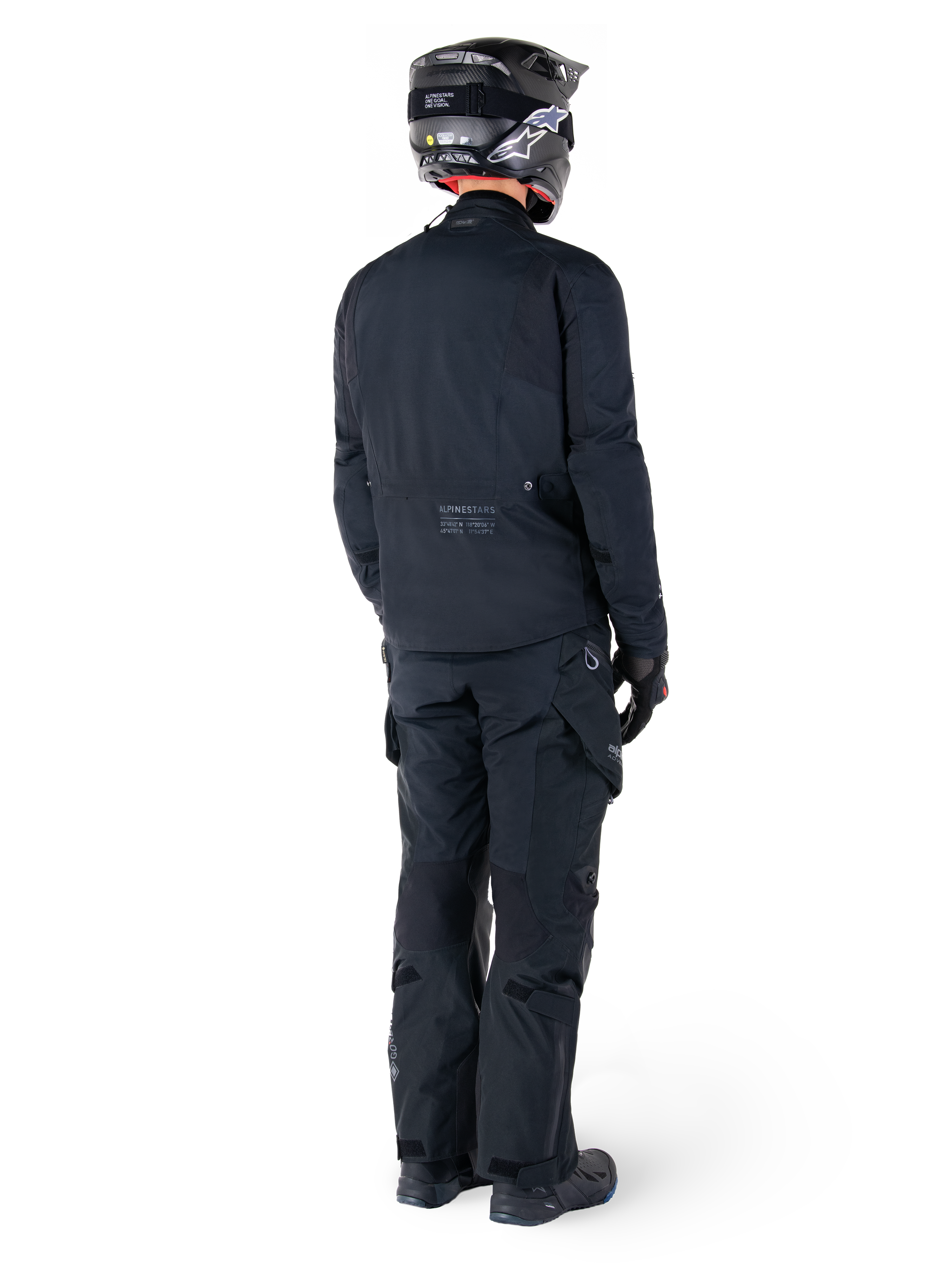 Set bagfra af en kører iført Alpinestars St-7 Prime GORE-TEX-jakke i sort, kombineret med matchende sorte touringbukser, sort motorcykelhjelm med hvidt logo og sorte motorcykelstøvler, komplet beskyttende adventure-udstyr til touring og pendling.