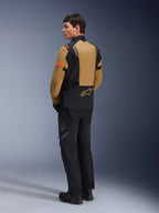 Alpinestars ST-7 2L GORE-TEX jakke, adventure-motorcykeljakke, Gobi Brown og sort, set bagfra på en model iført matchende kørebukser og støvler, med orange detaljer på ærmerne, vandtæt lamineret yderskal og Alpinestars-logo, designet til touring og landevejskørsel