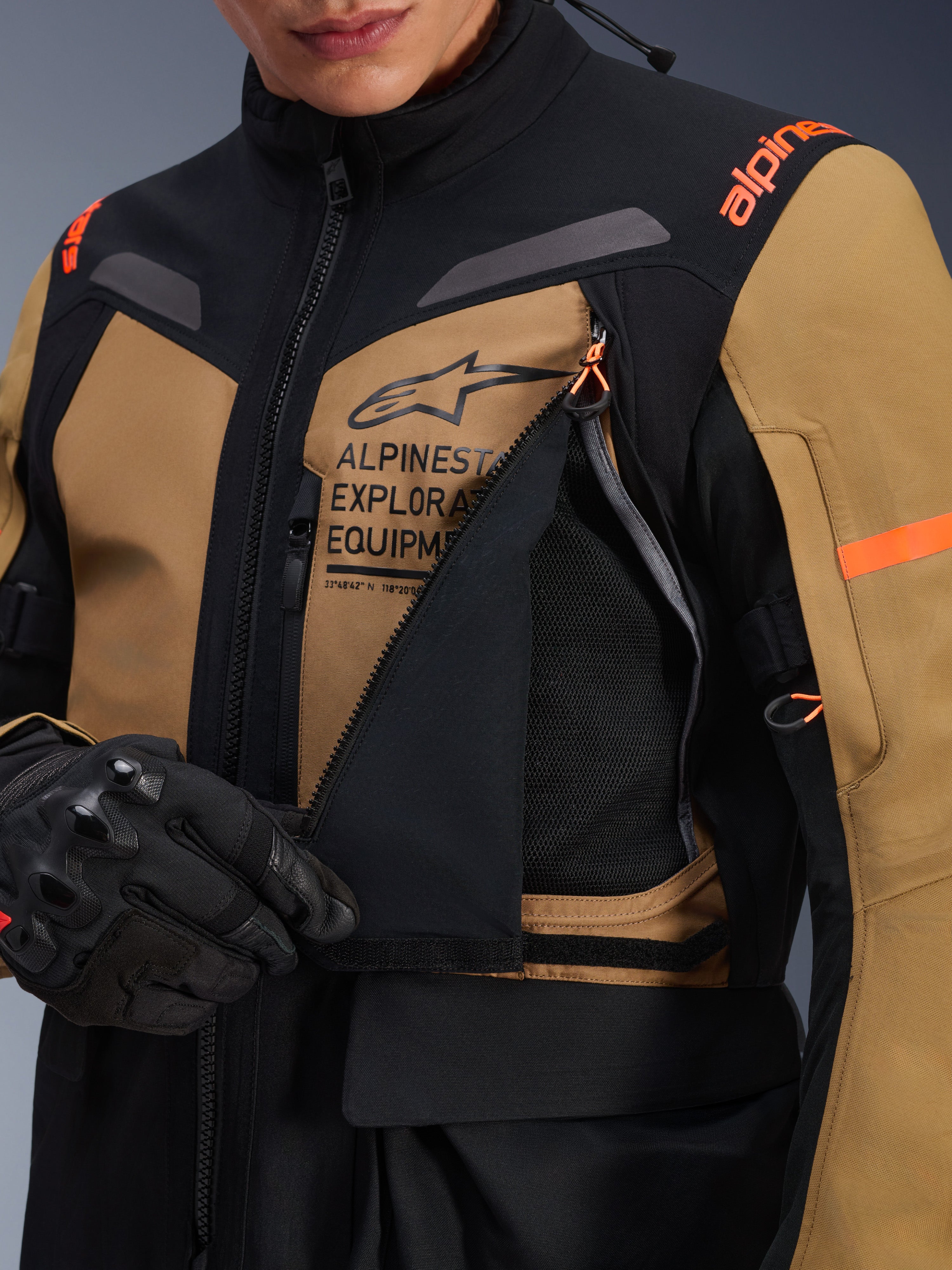 Alpinestars ST-7 2L GORE-TEX jakke, adventure touring motorcykeljakke, Gobi brun og sort, nærbillede af det åbne ventilationspanel på brystet, der afslører åndbart mesh, med Alpinestars Exploration Equipment branding og orange detaljer.
