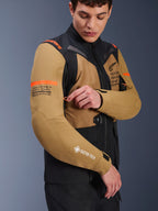 Alpinestars ST-7 2L GORE-TEX jakke i Gobi Brown og sort, adventure-touring motorcyke ljakke båre t af en mod el, der just erer en ven tilationsåbni ng på ærmet, med orange d etaljer, koo rdinatgrafik og GORE-TEX- logo