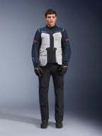 Alpinestars ST-7 2L GORE-TEX jakke, adventure touring motorcykeljakke, Ice Gray, mørkeblå og sort, båret med sorte bukser og handsker, med store cargolommer foran, røde detaljer på ærmerne og en lamineret GORE-TEX-skal for vandtæt ydeevne.