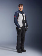 Alpinestars ST-7 2L GORE-TEX-jakke i farvekombinationen Ice Gray, Dark Blue og sort med røde detaljer, båret af en mandlig model med sorte motorcykelbukser og handsker, professionelt adventure touring-motorcykeludstyr