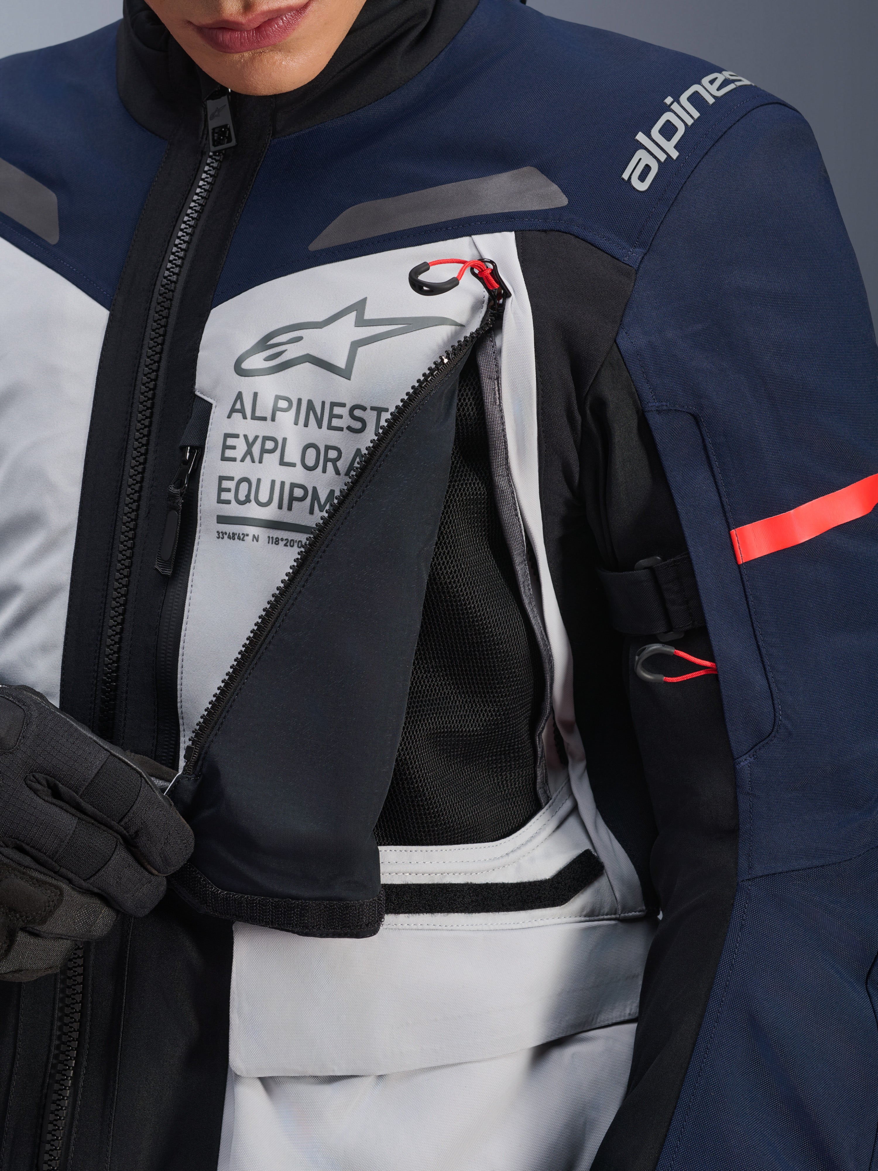 Alpinestars ST-7 2L GORE-TEX jakke, adventure touring-jakke, Ice Gray, mørkeblå og sort, detaljeret visning af det åbnede ventilationspanel på brystet, der afslører sort mesh, med Alpinestars Exploration Equipment-logo og røde detaljer på lynlåsstropperne