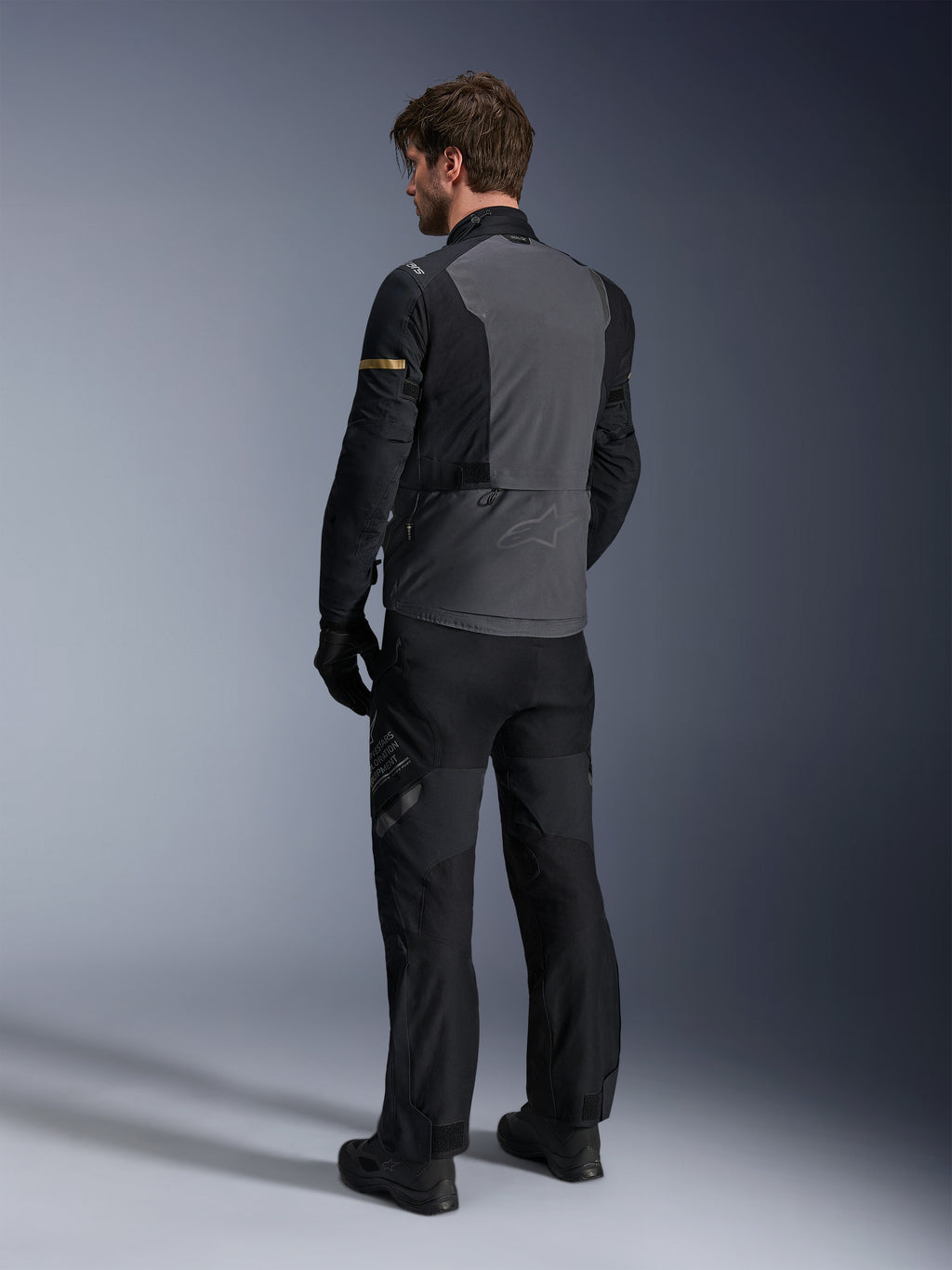 Alpinestars ST-7 2L GORE-TEX-jakke, adventure touring-udstyr, mørkegrå og sort med mørke khaki-detaljer, set bagfra af en kører iført jakken og matchende motorcykelbukser, vandtæt lamineret konstruktion