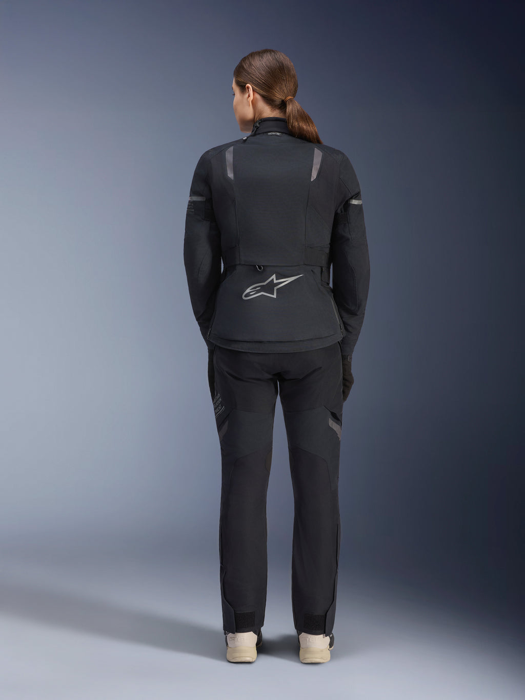 Alpinestars Dame Stella ST-7 2L GORE-TEX jakke, sort og mørkegrå, set bagfra med det sølvfarvede Alpinestars-logo på lænden, kombineret med matchende sorte tekstilbukser, adventure touring motorcykeludstyr