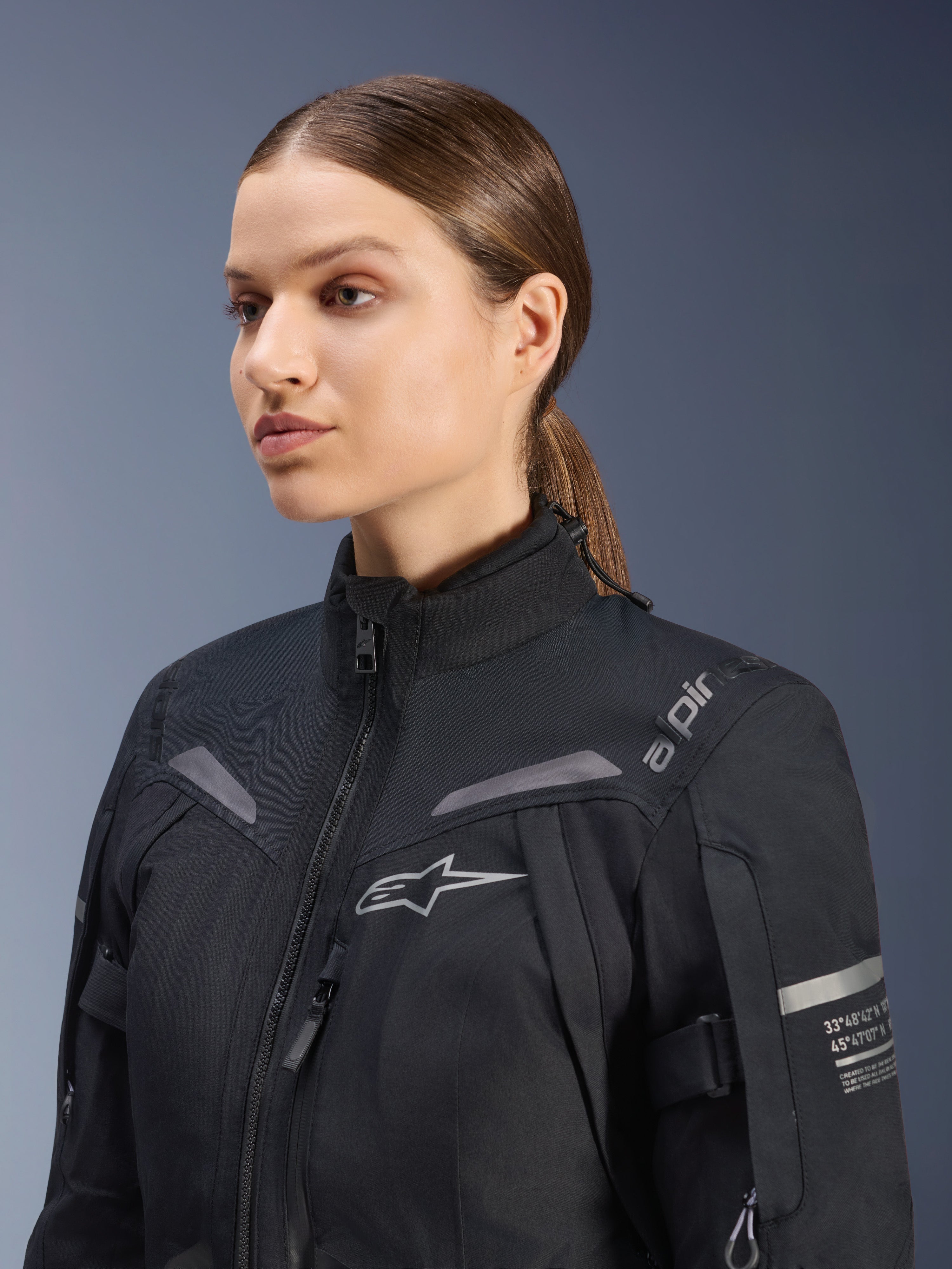 Alpinestars Stella ST-7 2L GORE-TEX damejakke, sort, med brystlogo og tekniske koordinater på armen, vandtæt tekstildesign med høj krave til motorcykel-touring, studioportræt af en kvindelig rytter.