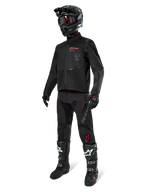 Motocross-kører i komplet racerudstyr, Alpinestars Pro-Dura-jakke i sort, sorte bukser med grå branding og røde detaljer, sort hjelm med goggles og sort-hvide motocross-støvler, koordineret outfit til enduro- og off-road-kørsel
