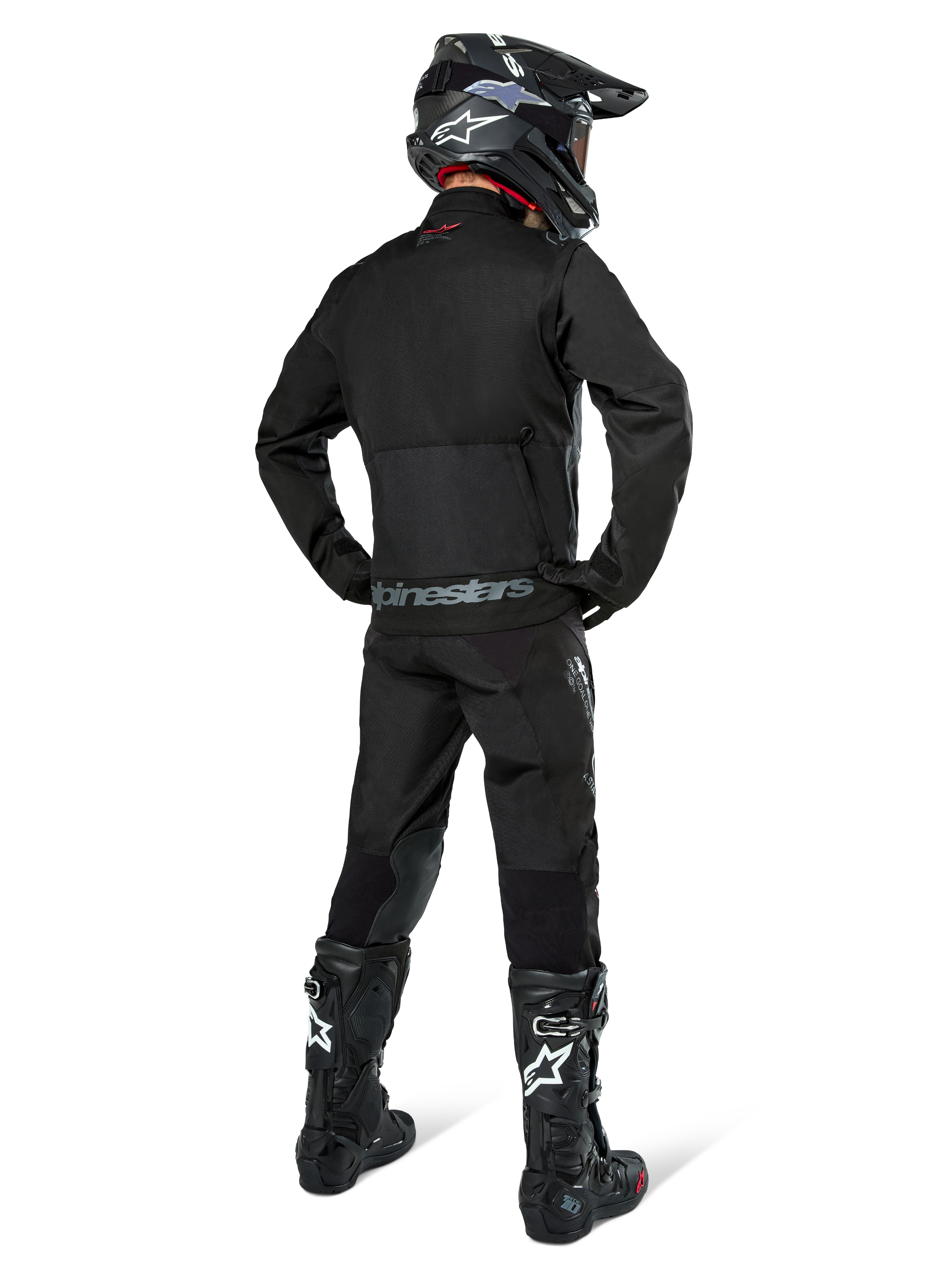 Alpinestars Pro-Dura jakke, sort off-road enduro-jakke, set bagfra båret med matchende bukser og sorte Tech 10-støvler, med fremtrædende Alpinestars-branding på den nederste del af ryggen, robust tekstilkonstruktion til aggressiv trail-kørsel