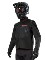 Alpinestars Pro-Dura jakke, off-road motorcykeljakke, sort med røde og grå logoer, har forlommer med lynlås og høj krave, bæres med en sort motocrosshjelm og handsker til enduro-løb